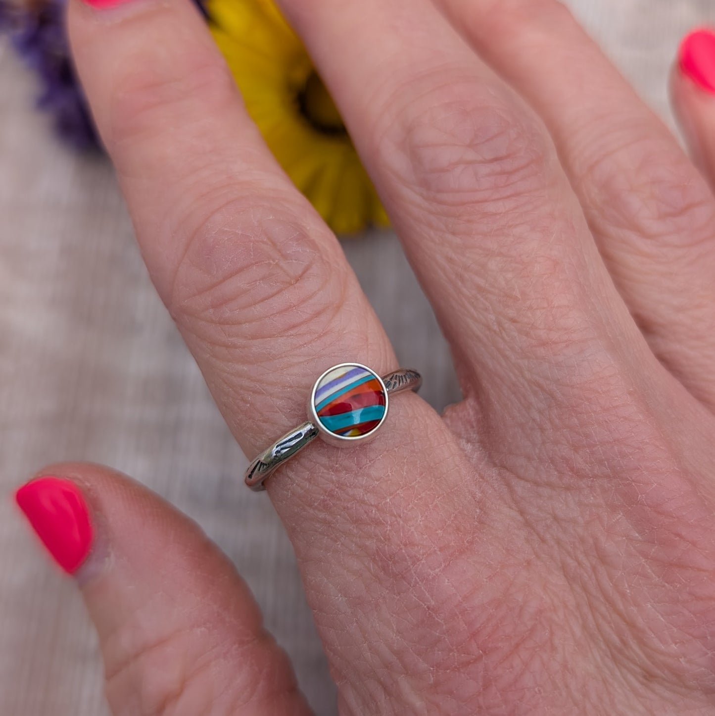Surfite Ring with Sunburst Stamp worn on a finger, showing a small round colourful Surfite stone in a handmade recycled sterling silver setting.