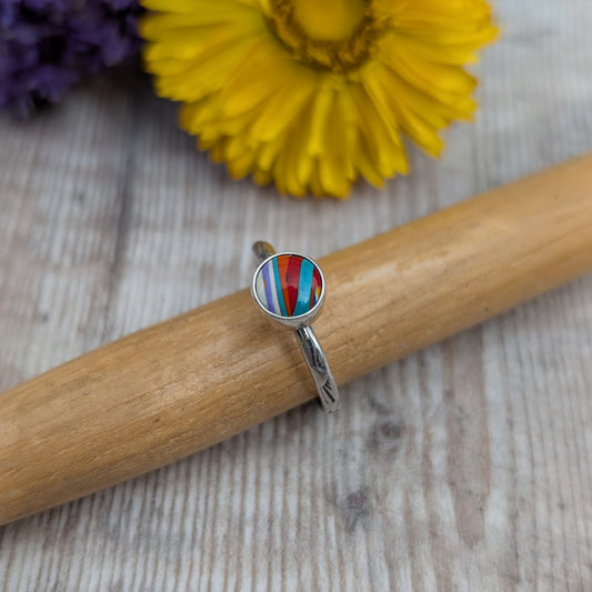 Surfite Ring with Sunburst Stamp resting on a wooden mandrel, highlighting the handmade recycled sterling silver band and colourful Surfite stone.