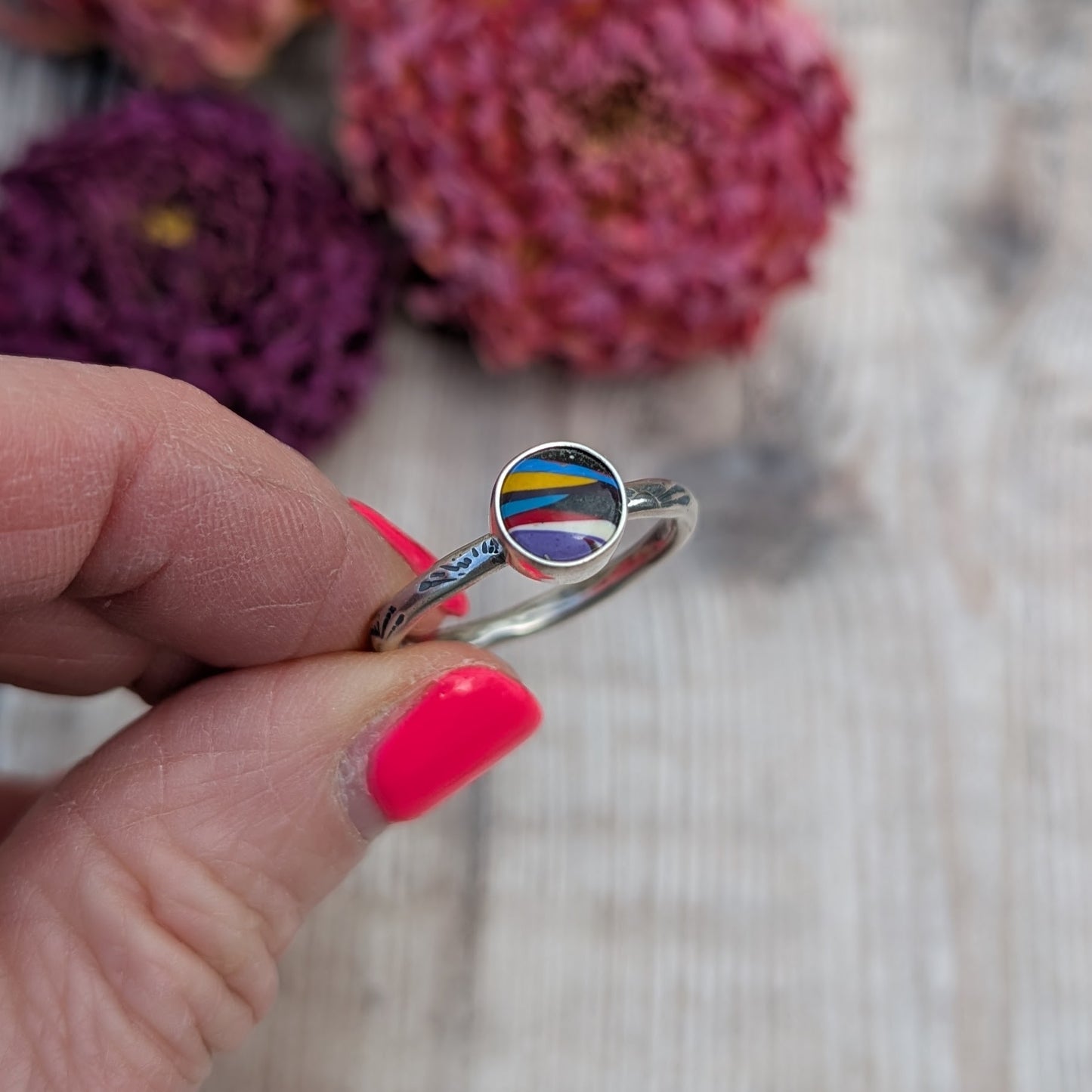 Surfite Ring with Sunburst Stamp held between fingers showing colourful round Surfite stone and stamped silver band