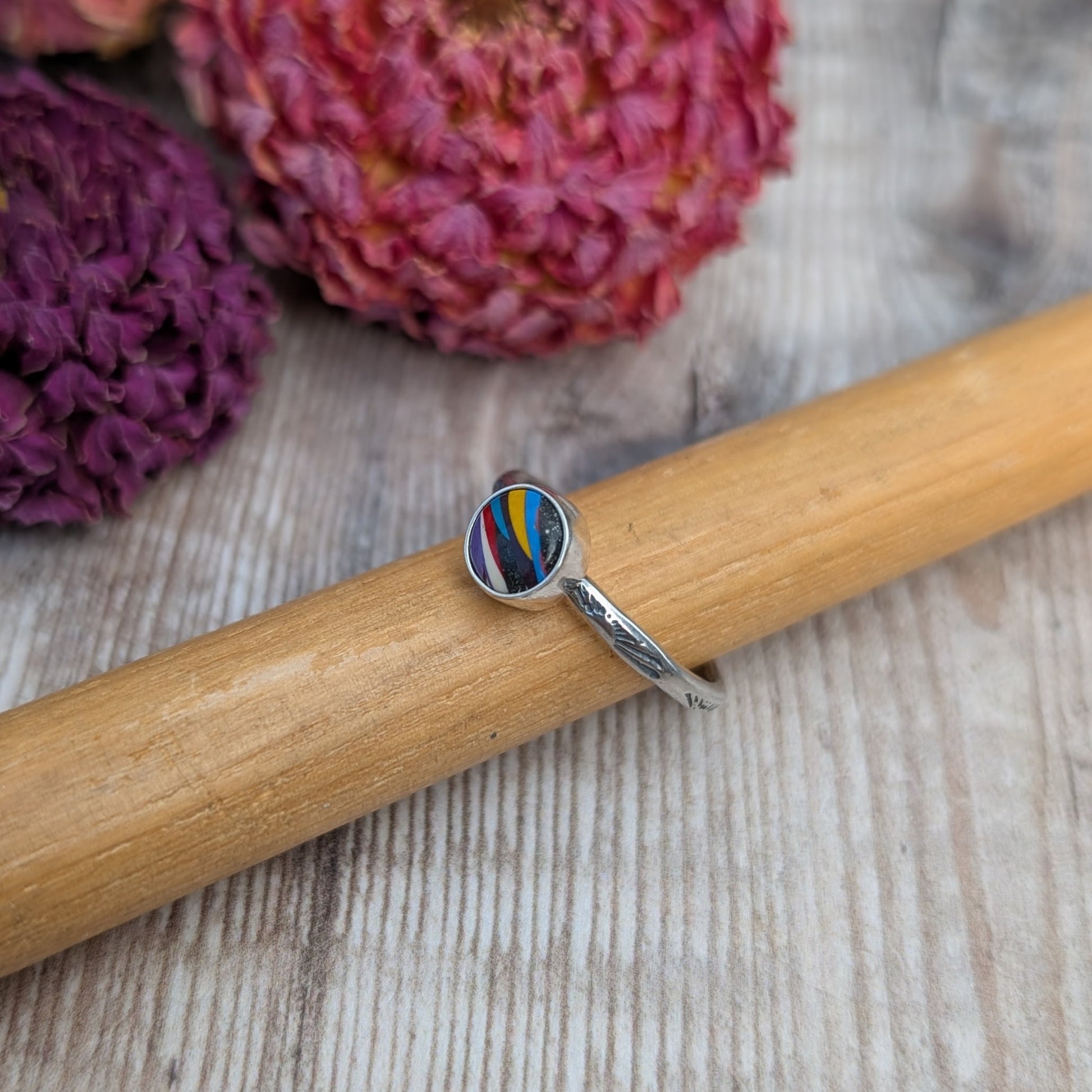 Surfite Ring with Sunburst Stamp resting on wooden ring mandrel with dried flowers in background