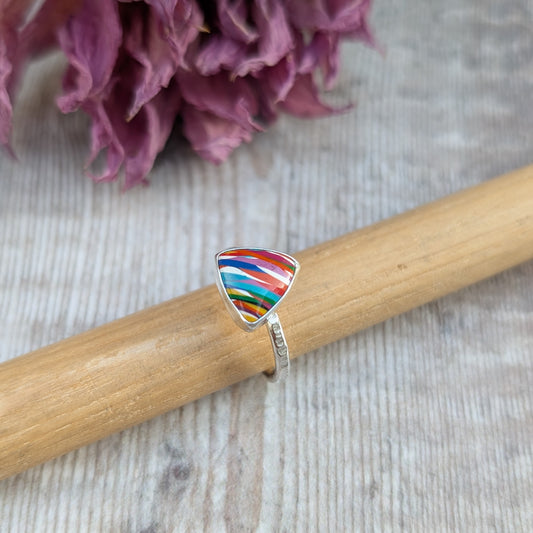 Sterling Silver triangular shaped surfite ring, UK Size 0. Resin stone has rounded edges and gloss finish. Set in a silver bezel, mounted on textured silver ring band approximately 2 mm wide. Resin colours in uneven stripes include red, blue, orange, turquoise, green and flecks of white.