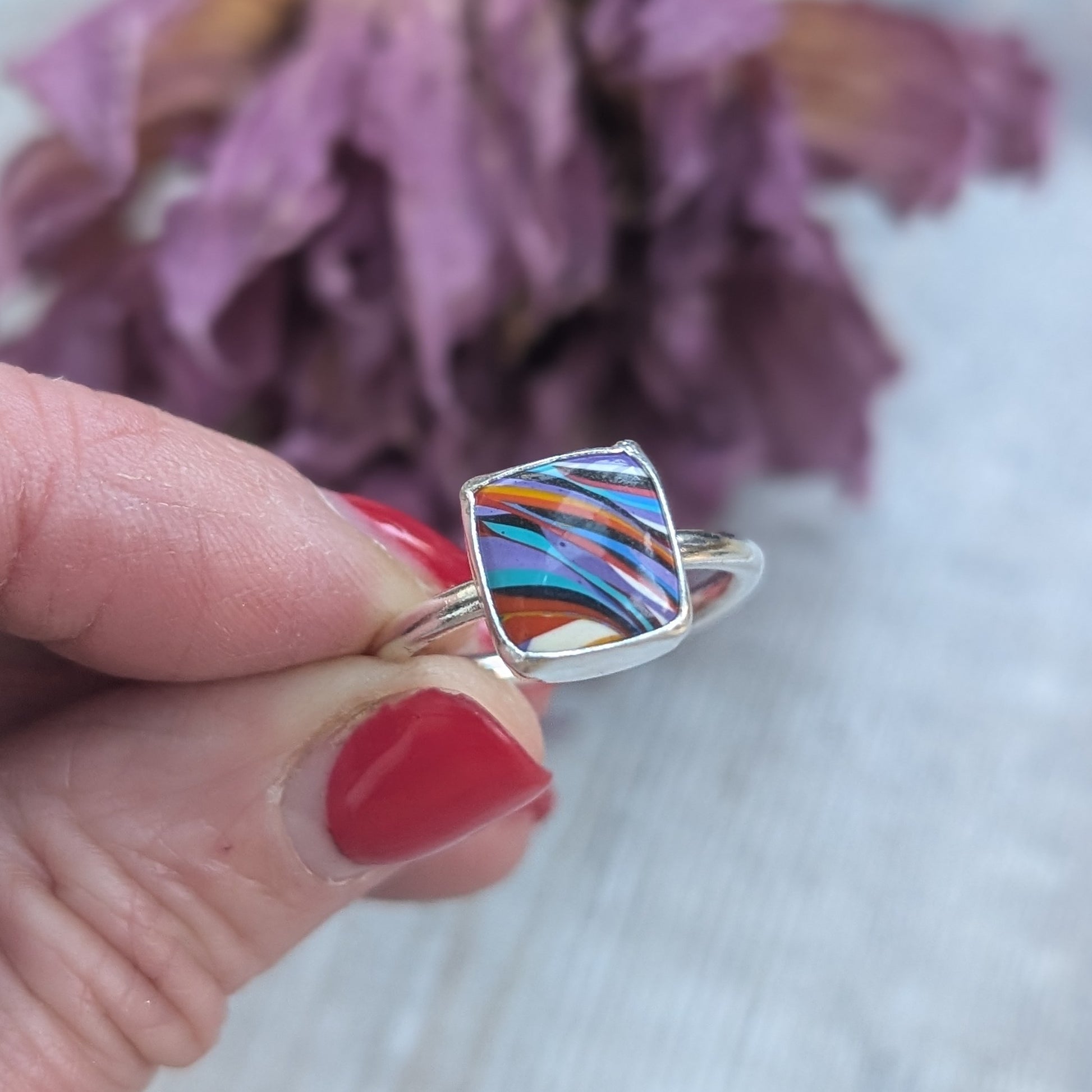 Sterling Silver square surfite resin stone with rounded edges and gloss surface measuring approximately 9 x 9mm. Set in a silver bezel and mounted on silver ring band approx 2 mm wide. Uneven diagonal stripes of colour are mainly orange, blue, black, white and yellow.