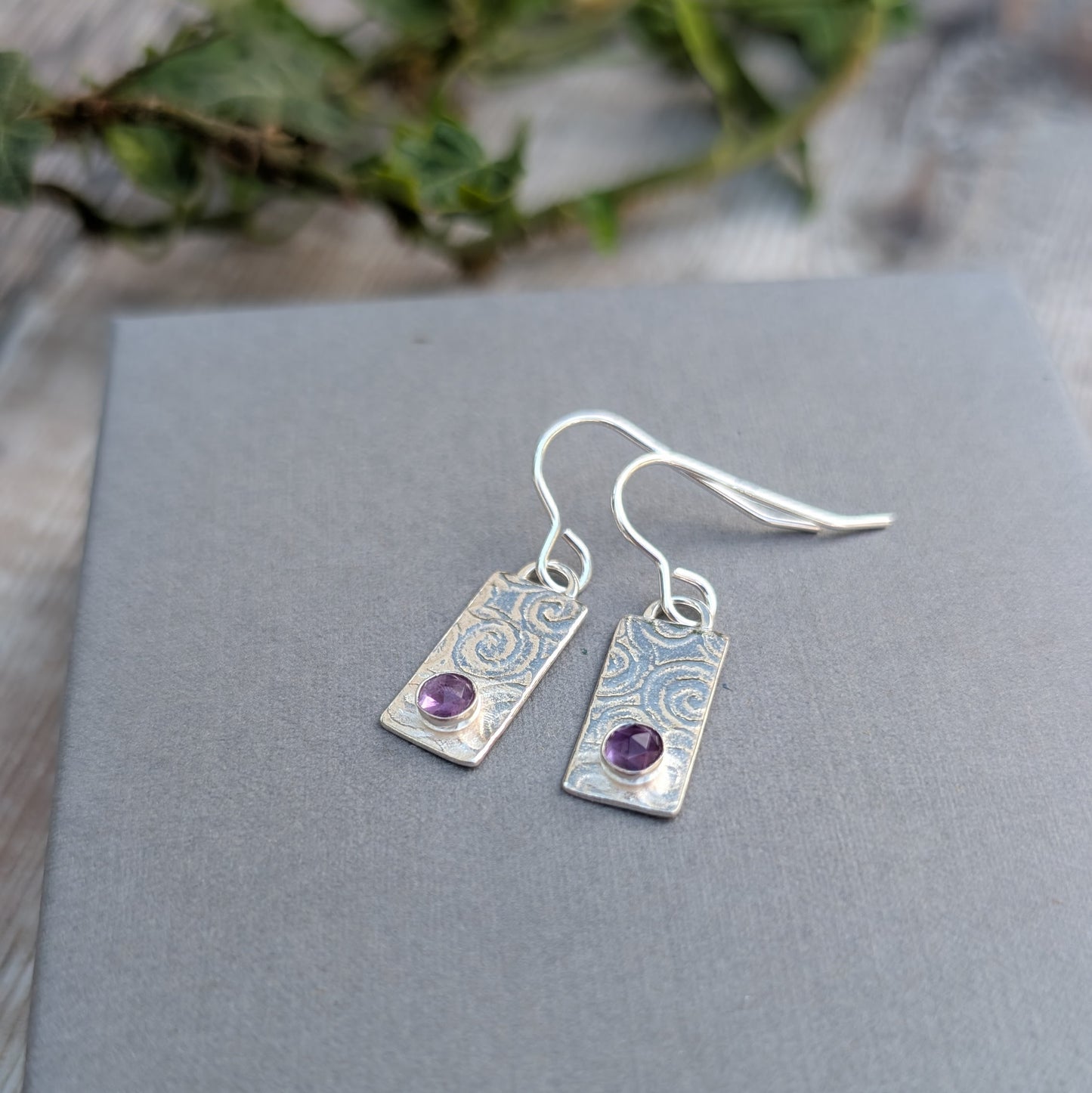 Swirly Rectangle Patterned Earrings with Amethyst handmade from recycled Sterling Silver, displayed on a grey card with a swirly stamped pattern and round purple Amethyst stones.