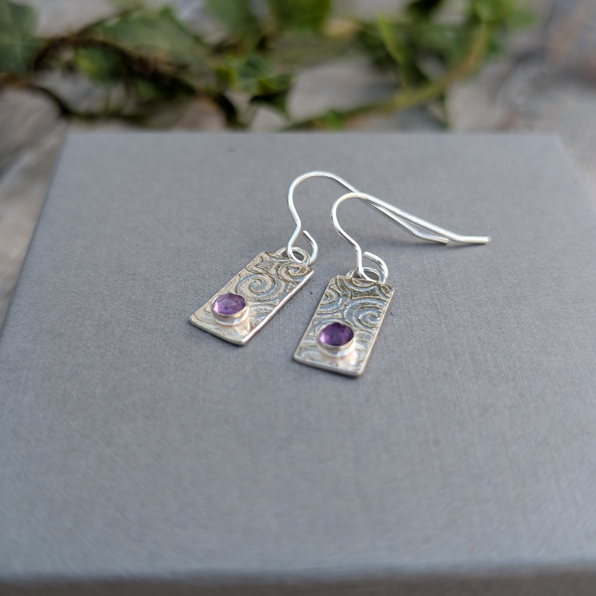 Swirly Rectangle Patterned Earrings with Amethyst made from recycled Sterling Silver, photographed on a grey display card, showing the hand-stamped swirly pattern and faceted Amethyst stones.