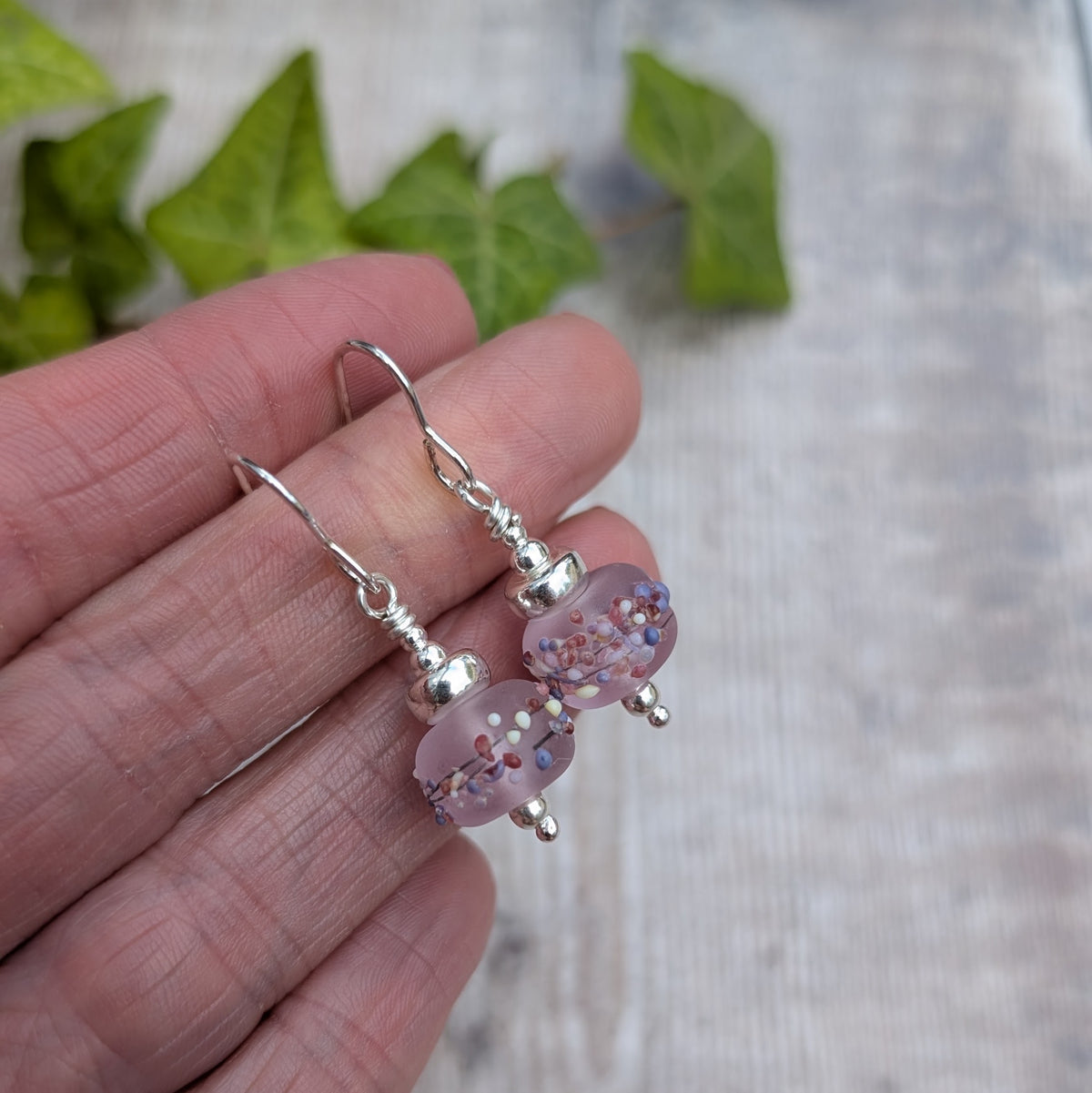 Tropical Pink Lampwork Glass Earrings held in a hand, showing the recycled Sterling Silver ear wires and handmade pink glass beads.