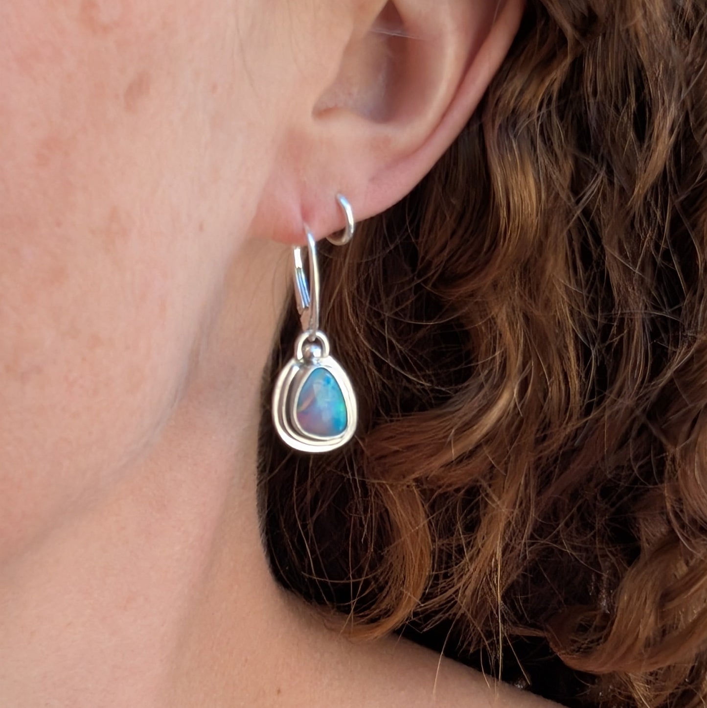 Turquoise Blue Aurora Opal Teardrop Earrings worn on the ear, handmade from recycled Sterling Silver with vibrant blue and green Aurora Opals.