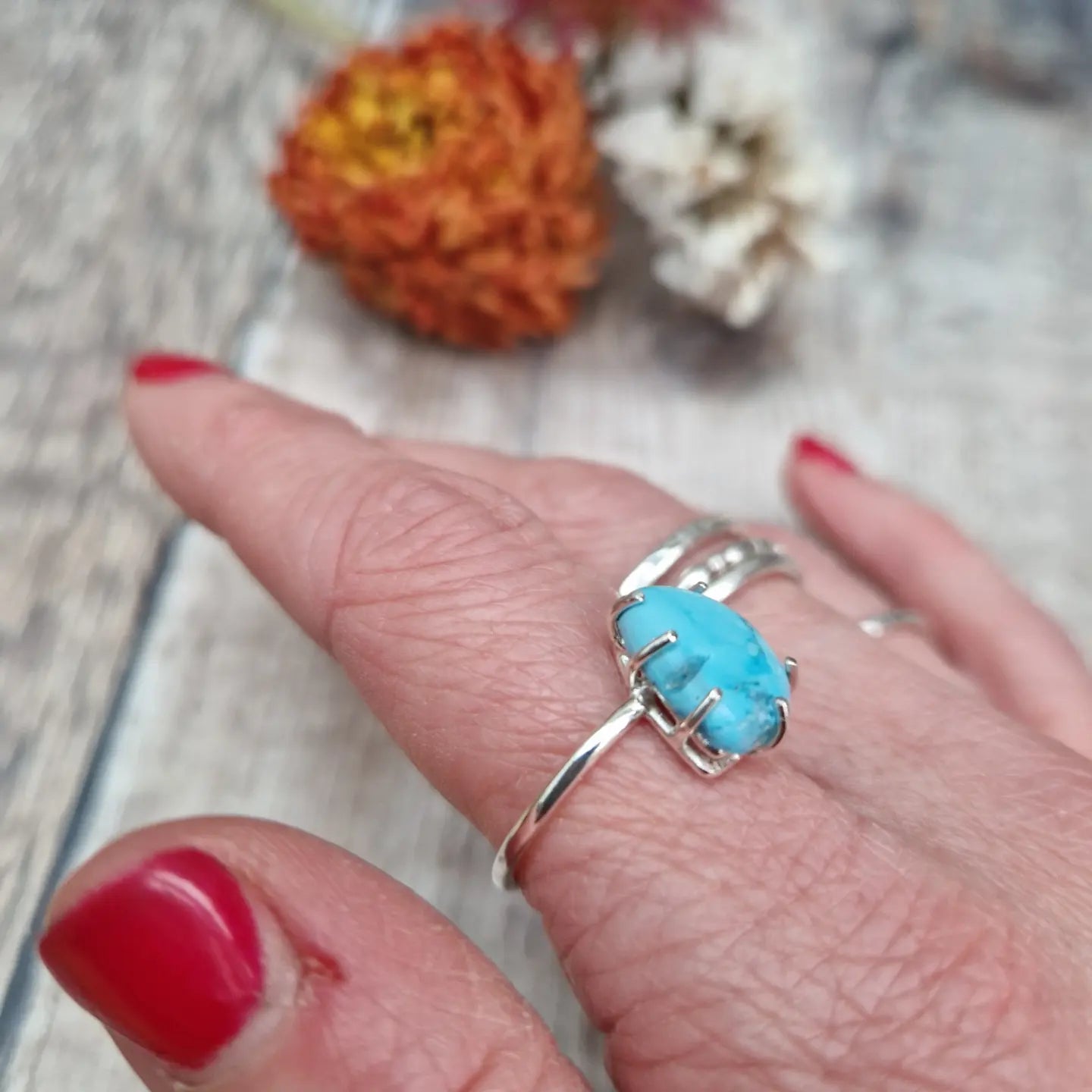 Turquoise teardrop shaped gemstone set in silver claw bezel mounted on top of a Sterling Silver band approx. 2mm wide. The light-coloured turquoise stone has marbling effects of deeper blues running through it and is mounted at an angle to the band.