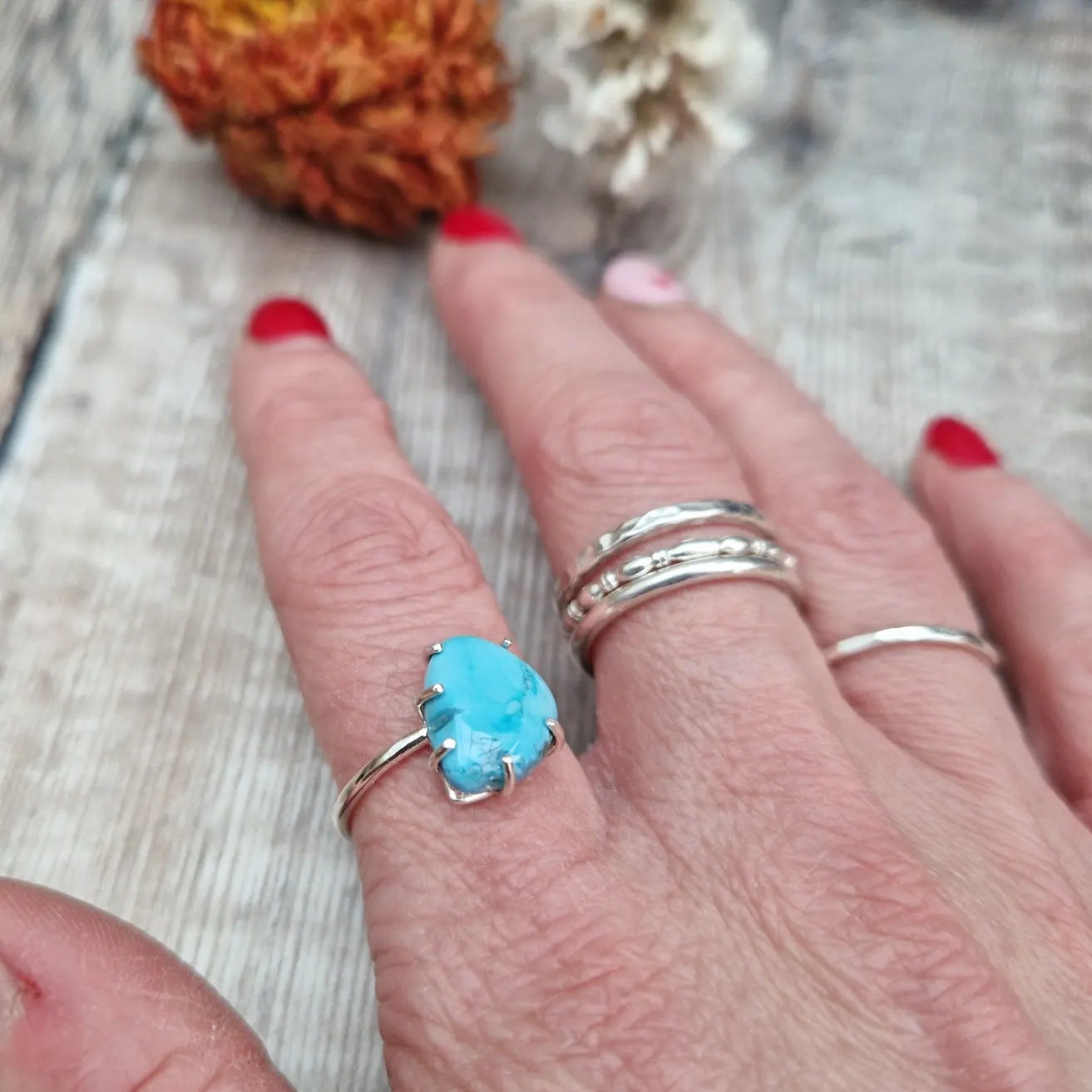 Turquoise teardrop shaped gemstone set in silver claw bezel mounted on top of a Sterling Silver band approx. 2mm wide. The light-coloured turquoise stone has marbling effects of deeper blues running through it and is mounted at an angle to the band.