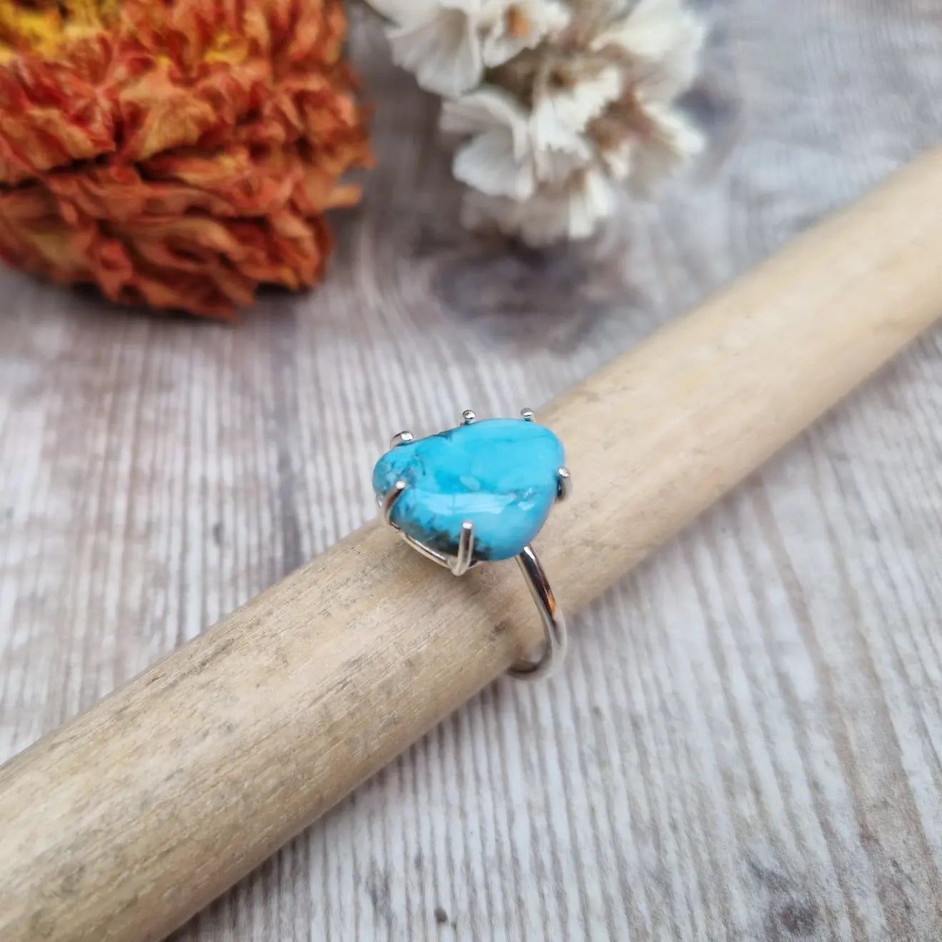 Turquoise teardrop shaped gemstone set in silver claw bezel mounted on top of a Sterling Silver band approx. 2mm wide. The light-coloured turquoise stone has marbling effects of deeper blues running through it and is mounted at an angle to the band.