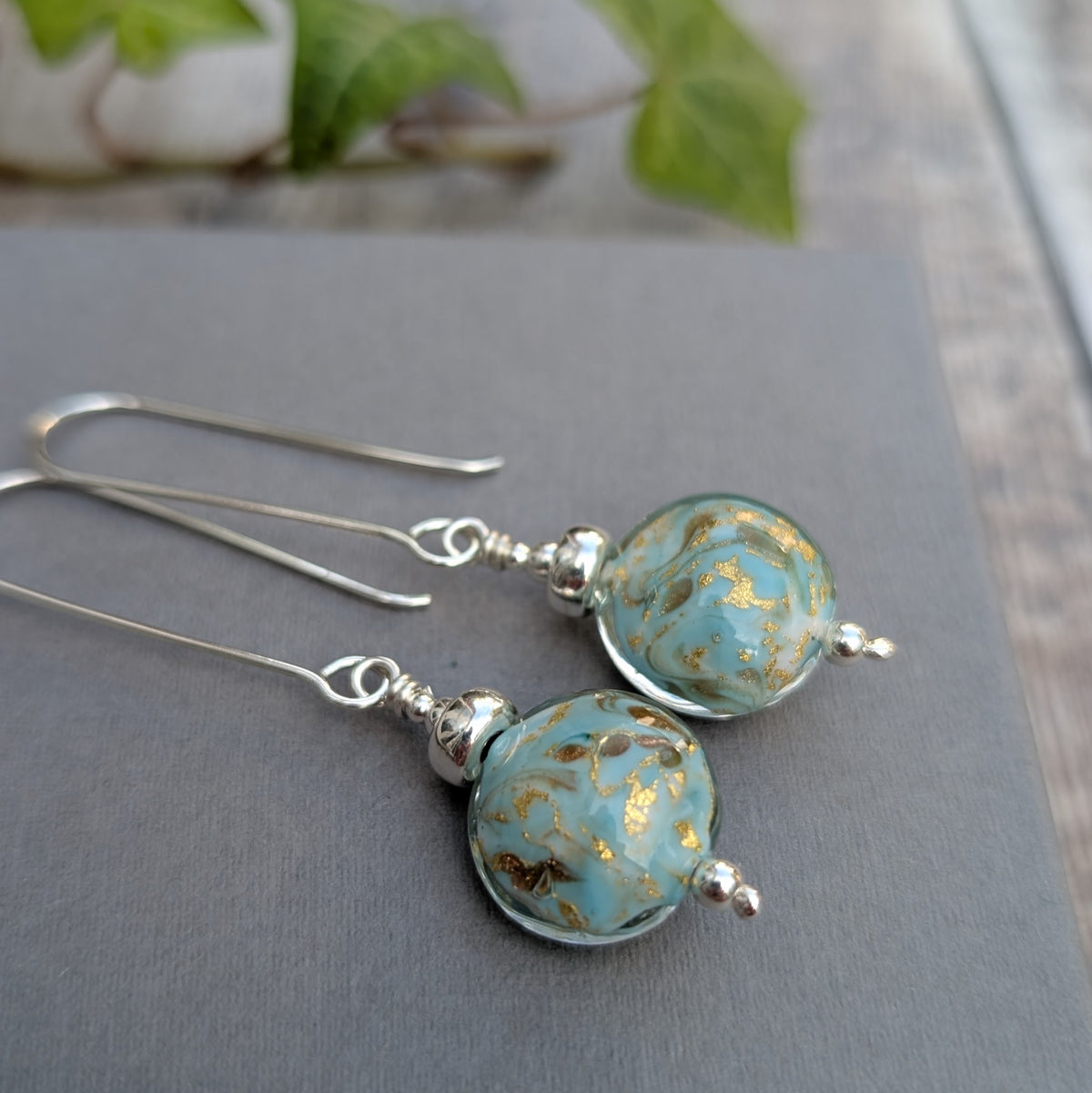 Close up of turquoise marbled Venetian glass long silver earrings, showing the handmade turquoise glass beads with gold marbled details.