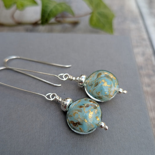 Close up of turquoise marbled Venetian glass long silver earrings, showing the handmade turquoise glass beads with gold marbled details.