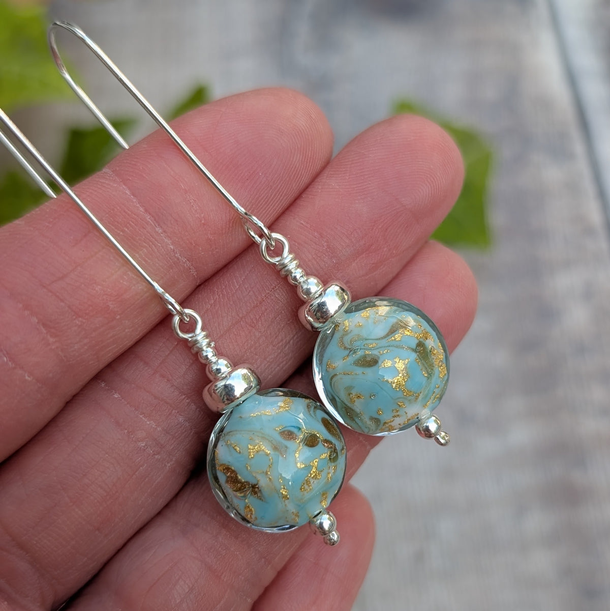 turquoise marbled Venetian glass long silver earrings held in a hand, showing the round handmade lampwork glass beads and silver details.
