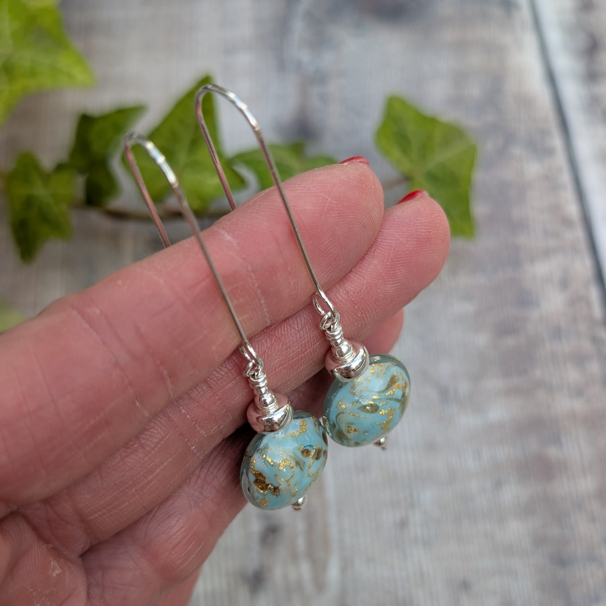 Side view of turquoise marbled Venetian glass long silver earrings held in a hand, showing the handmade glass beads and long silver ear wires.
