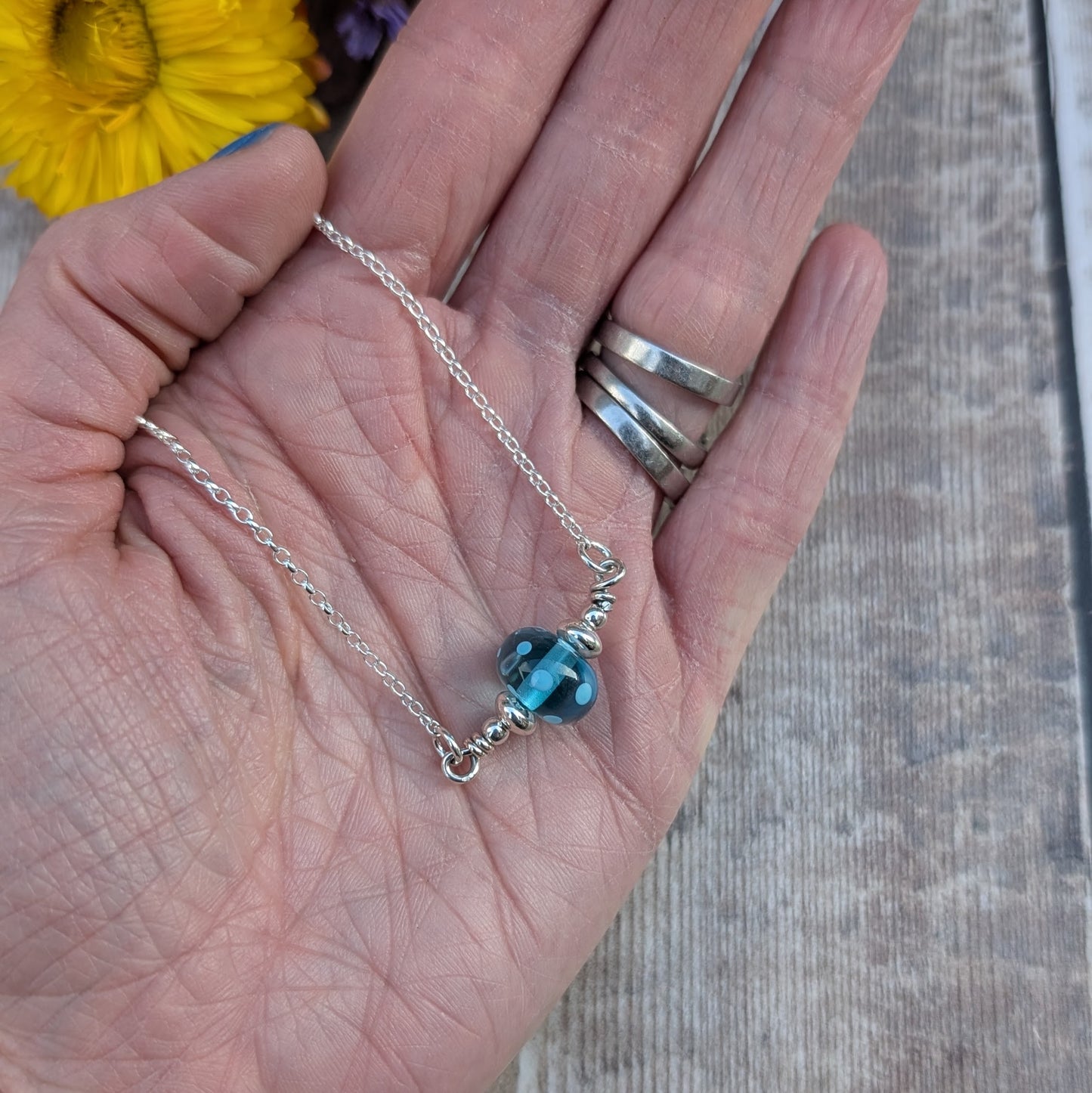 Silver chain necklace featuring a turquoise colour lampwork glass bead with subtle internal spots as details. The bead is accented with small silver beads to each side and is suspended between the chain via two small open circle links on either side.