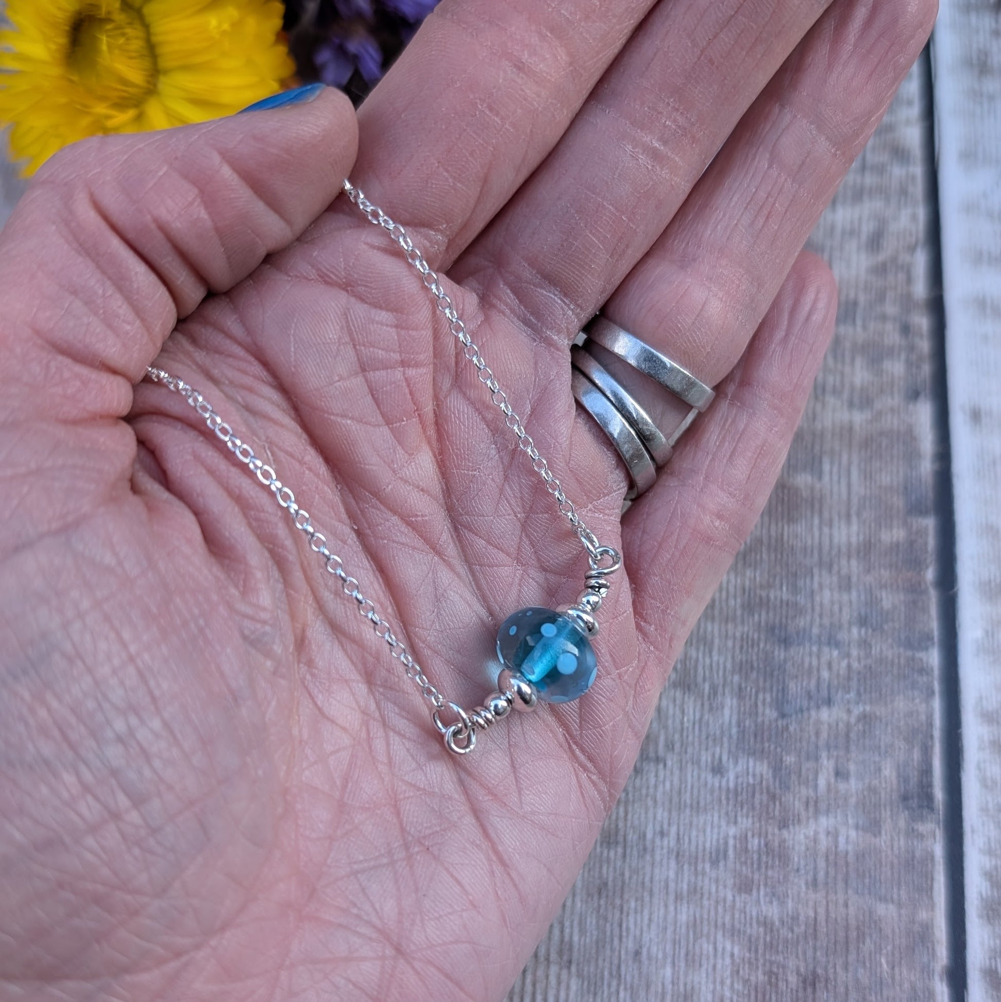 Silver chain necklace featuring a turquoise colour lampwork glass bead with subtle internal spots as details. The bead is accented with small silver beads to each side and is suspended between the chain via two small open circle links on either side.