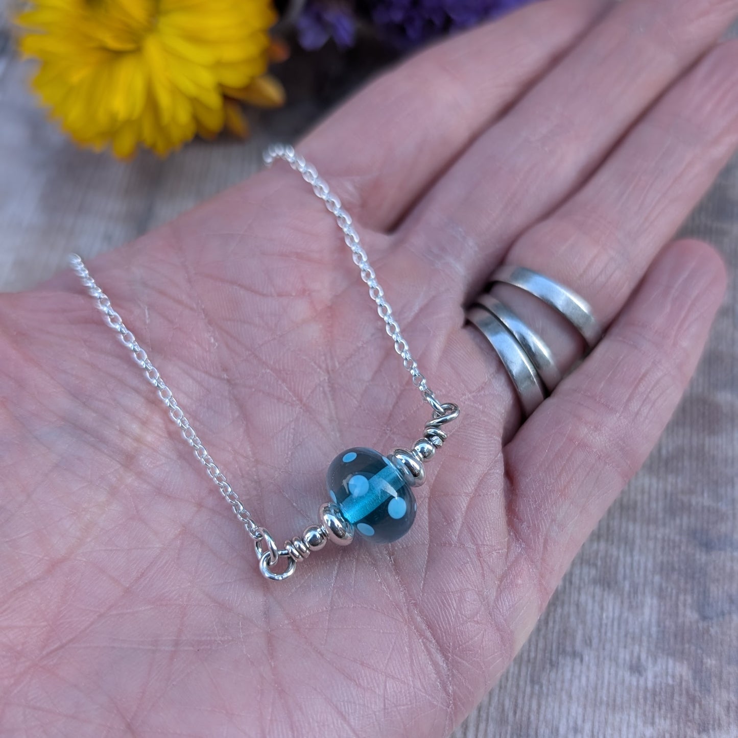 Silver chain necklace featuring a turquoise colour lampwork glass bead with subtle internal spots as details. The bead is accented with small silver beads to each side and is suspended between the chain via two small open circle links on either side.