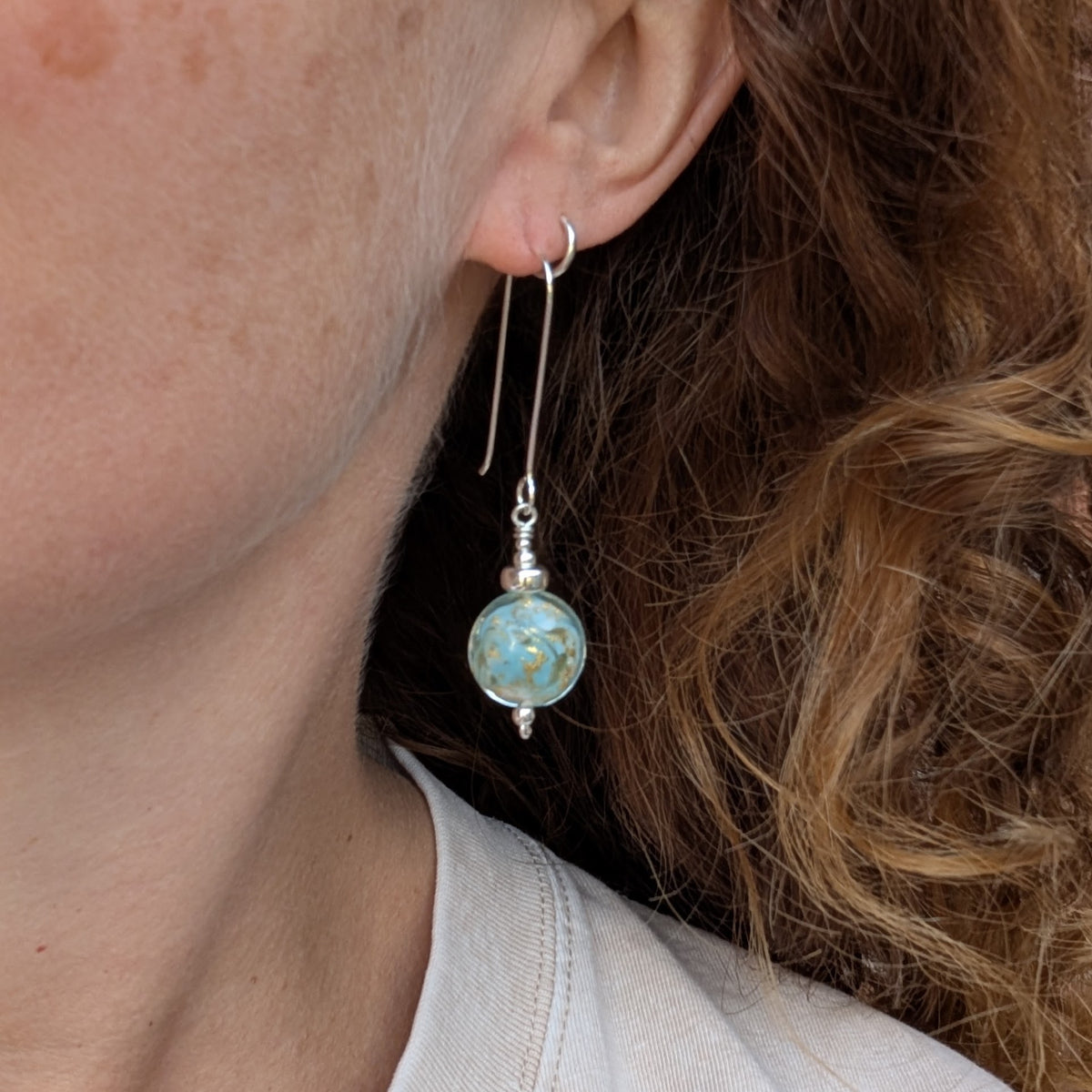 turquoise marbled Venetian glass long silver earrings being worn, showing the length of the silver ear wire and turquoise lampwork glass bead.