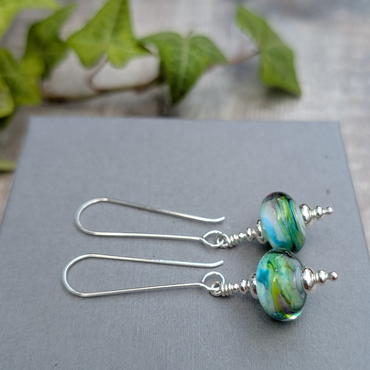 Watercolour Lampwork Glass Long Earrings handmade from recycled Sterling Silver with blue, green, yellow and white Lampwork glass beads, displayed on a grey background.