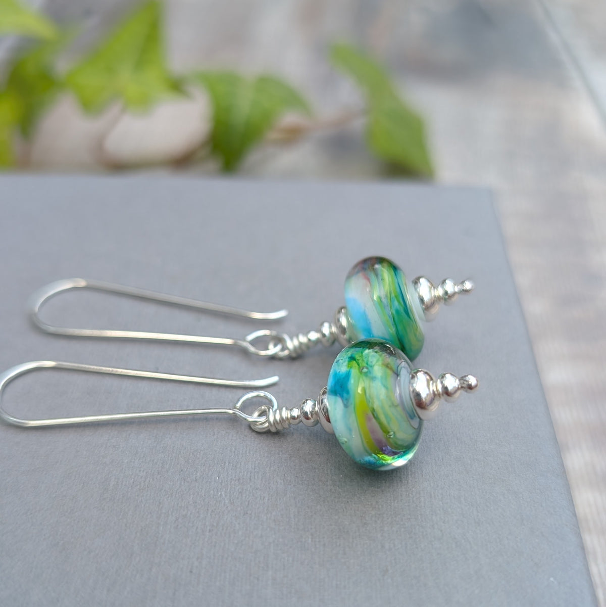 Watercolour Lampwork Glass Long Earrings handmade from recycled Sterling Silver with blue, green and yellow handmade glass beads, shown close up on a grey background.