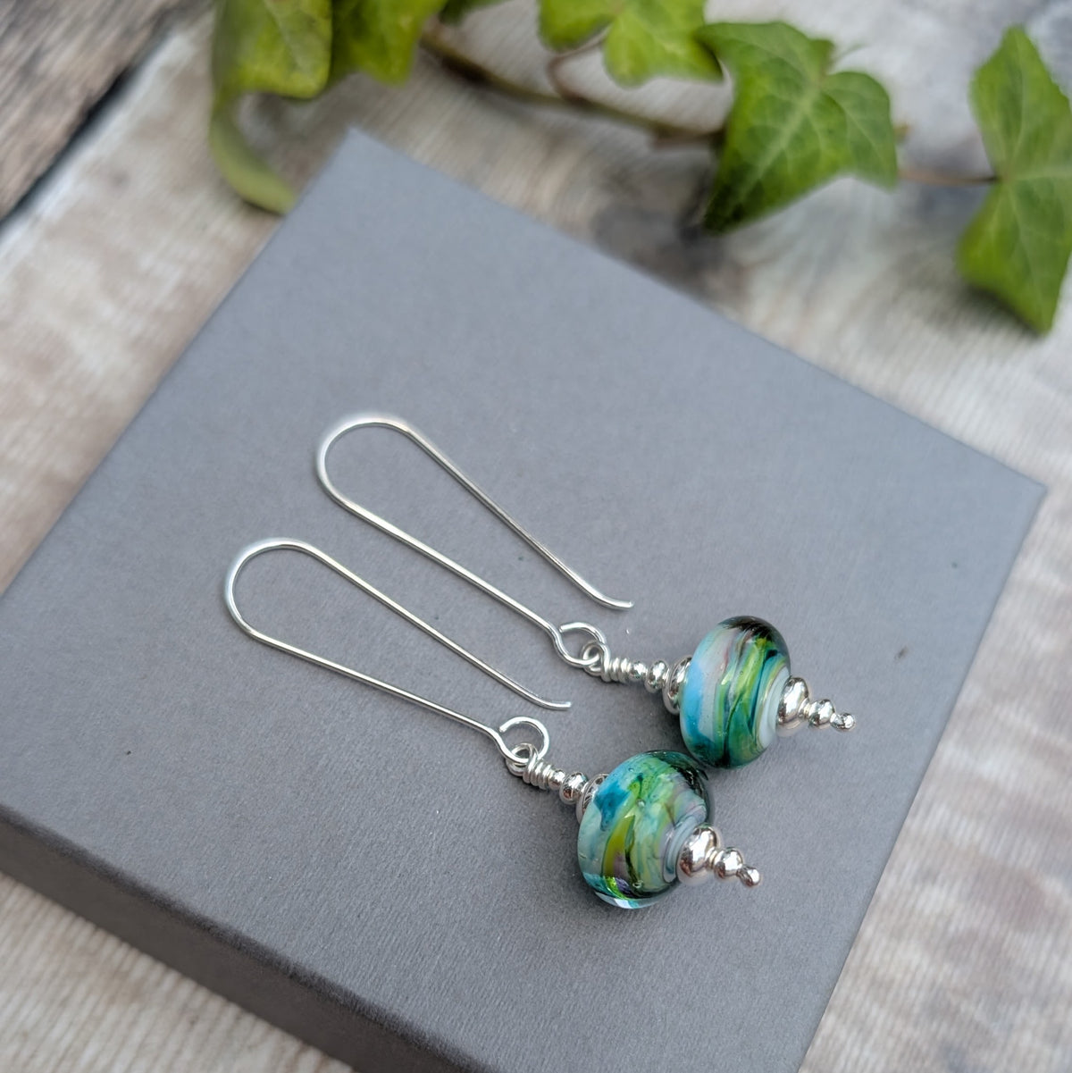 Watercolour Lampwork Glass Long Earrings with handmade blue, green and yellow Lampwork glass beads and long recycled Sterling Silver ear wires, displayed on a grey box.