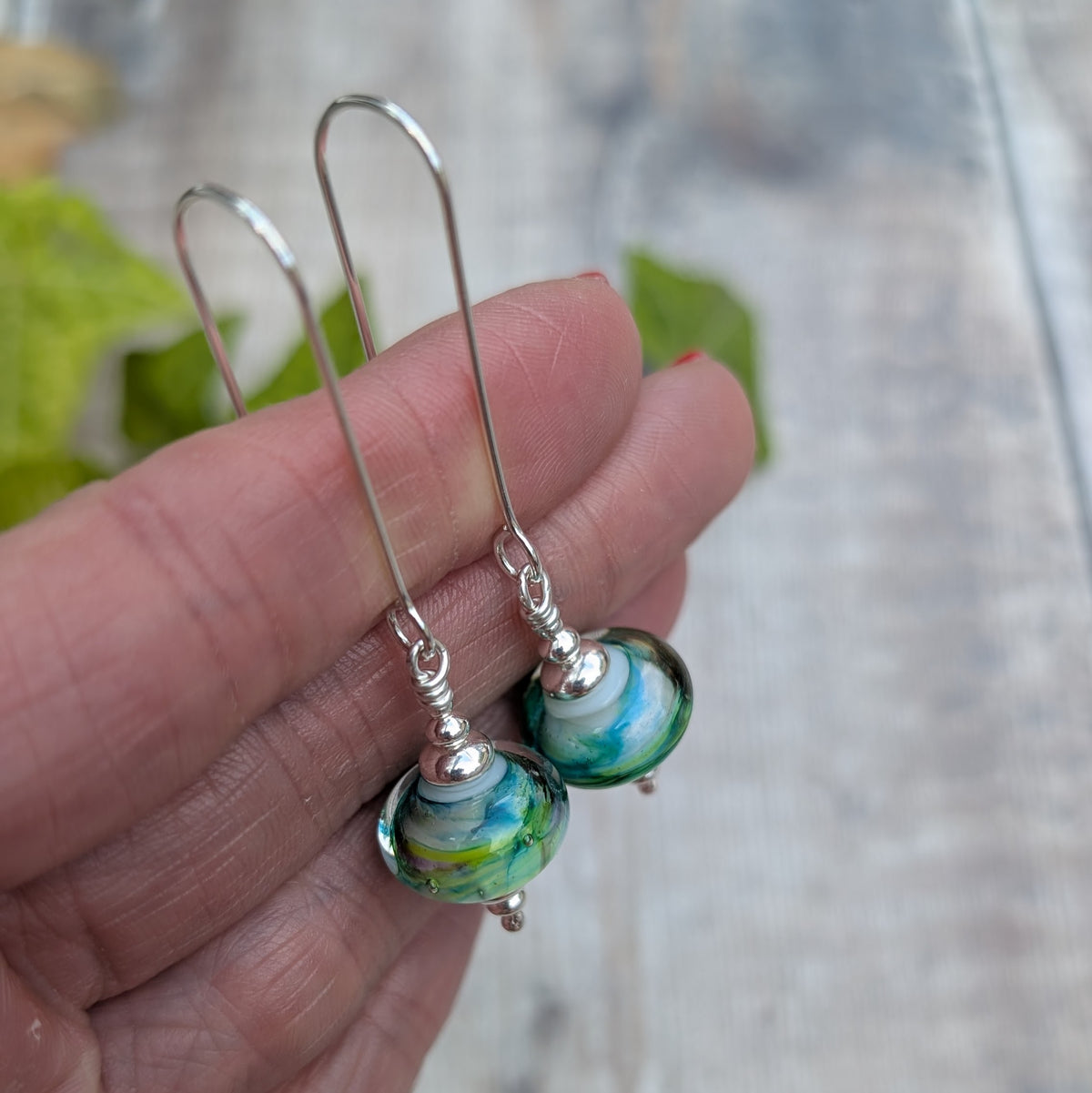 Close up of Watercolour Lampwork Glass Long Earrings held in a hand, showing the handmade glass beads and recycled Sterling Silver details.