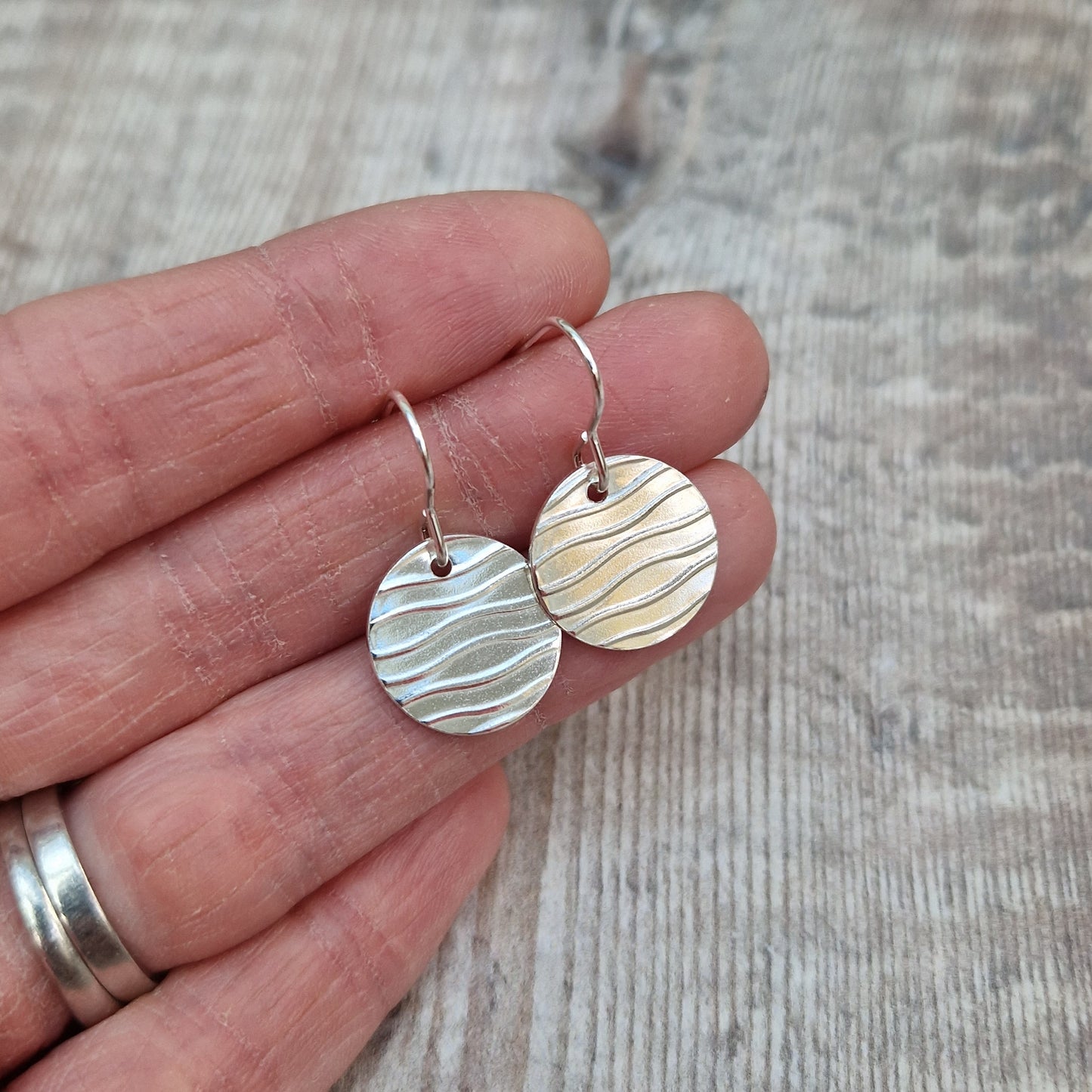 Each earring is a sterling silver disc stamped with a wavy line pattern. The wavy lines are spaced apart and raised from the disc, suspended from silver earring wire.