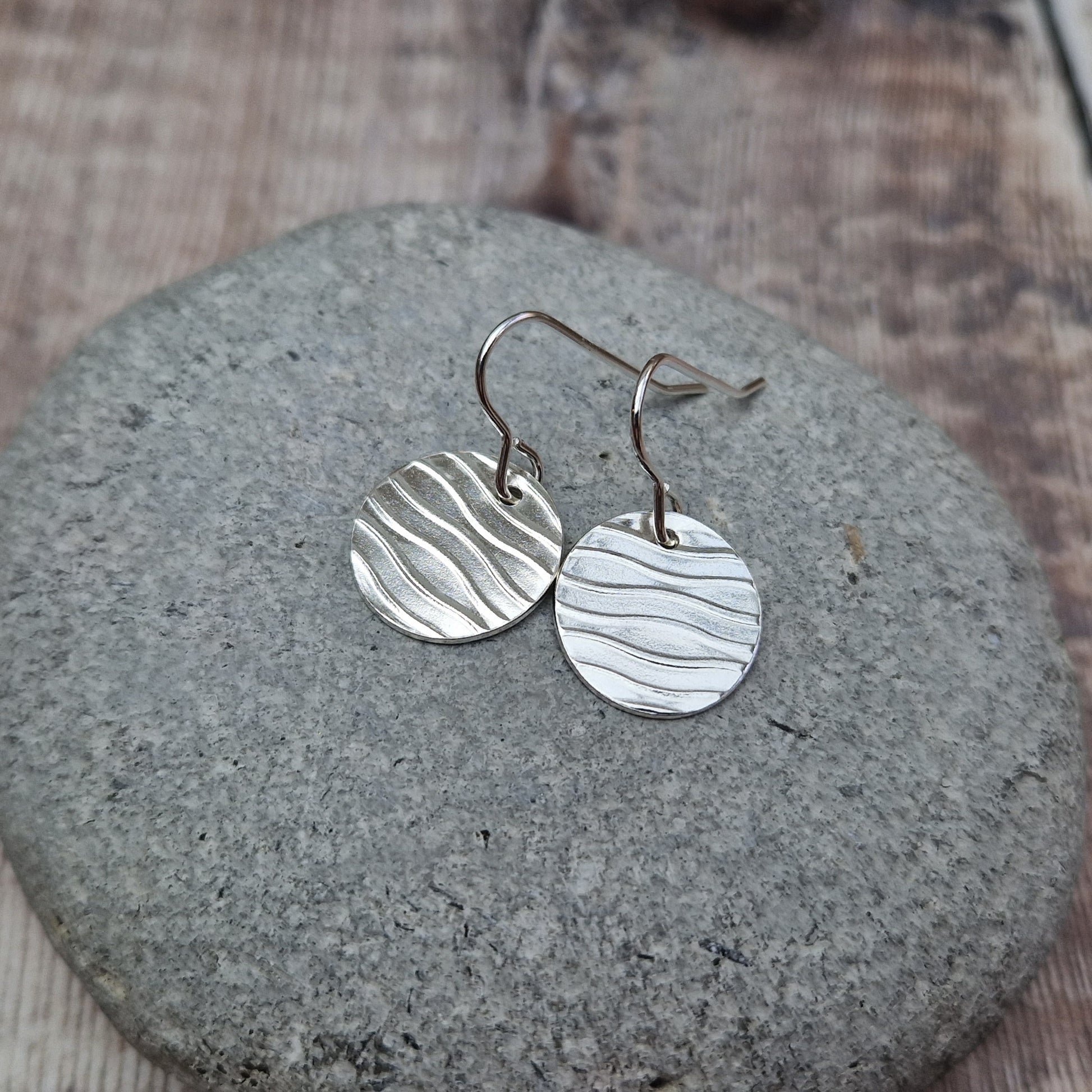 Each earring is a sterling silver disc stamped with a wavy line pattern. The wavy lines are spaced apart and raised from the disc, suspended from silver earring wire.