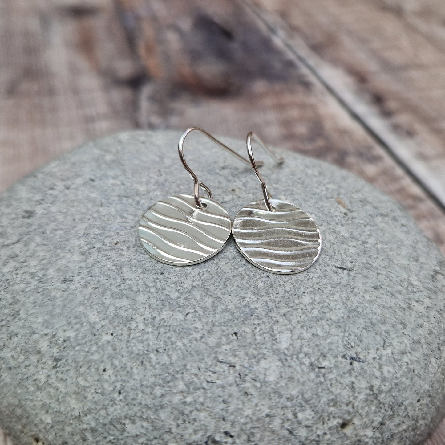 Each earring is a sterling silver disc stamped with a wavy line pattern. The wavy lines are spaced apart and raised from the disc, suspended from silver earring wire.