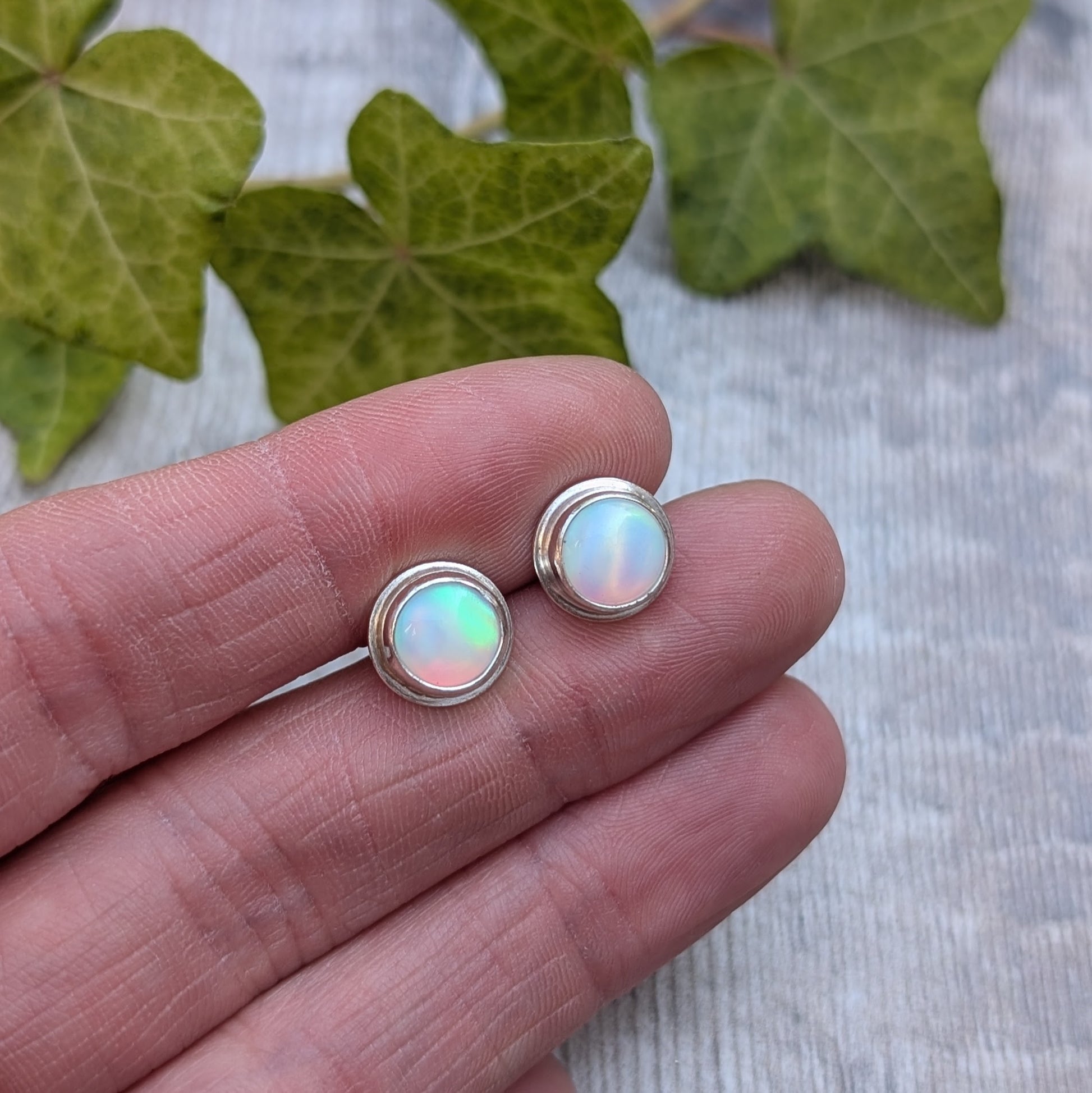 Close up of white aurora opal stud earrings handmade from recycled Sterling Silver, showing the soft flashes of pink, green and blue within the Aurora Opals.