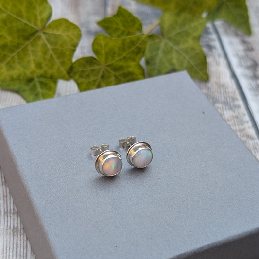 White aurora opal stud earrings handmade from recycled Sterling Silver displayed on a grey jewellery box with colourful Aurora Opals catching the light.