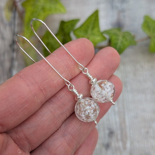 White aventurina Venetian glass long silver earrings handmade from recycled Sterling Silver, held in a hand showing the white and gold glass beads.