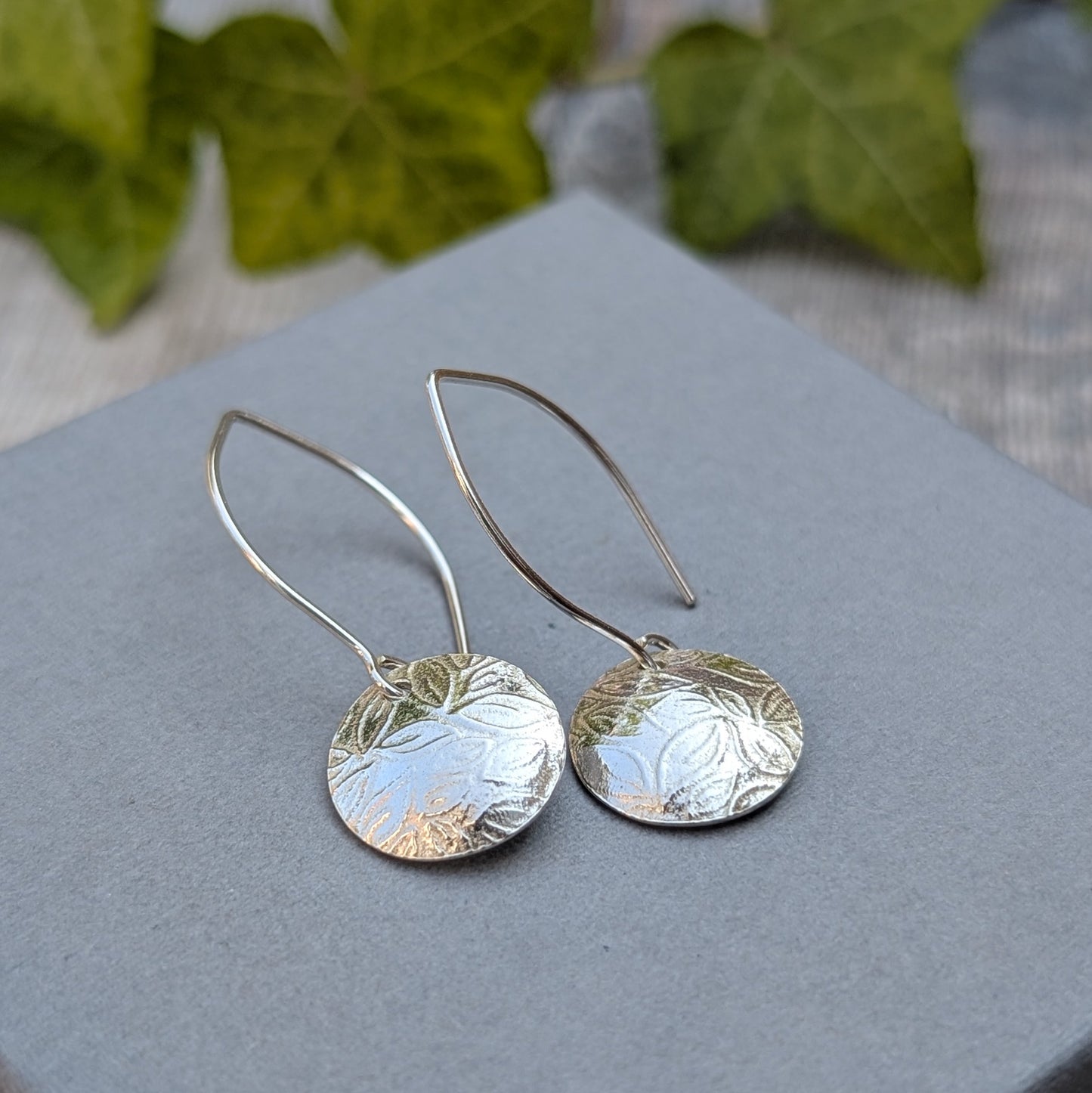 Close up of leaf pattern disc drop earrings handmade from recycled Sterling Silver showing the detailed leaf texture on the silver discs.