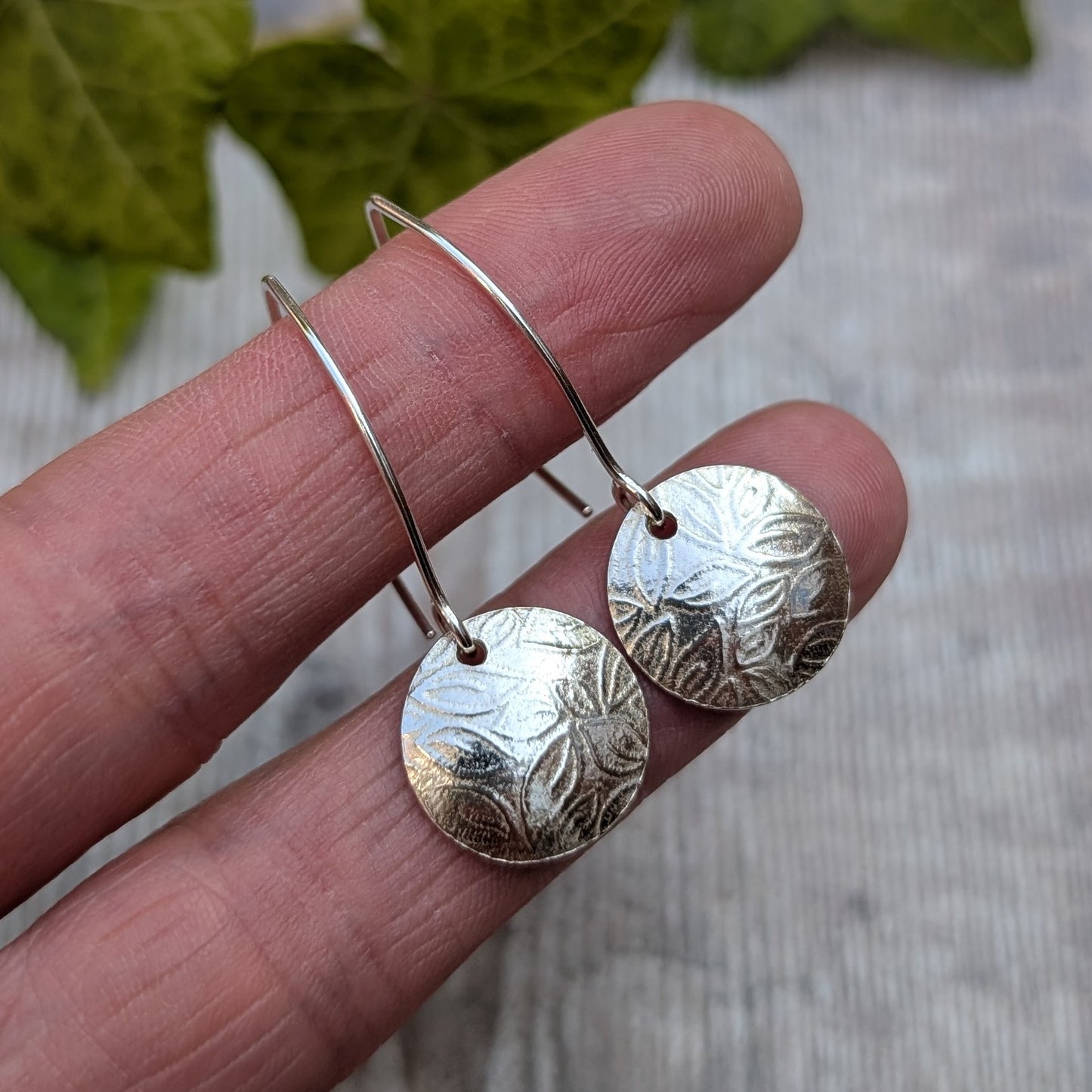 Close up of leaf pattern disc drop earrings handmade from recycled Sterling Silver highlighting the detailed leaf pattern and polished finish.