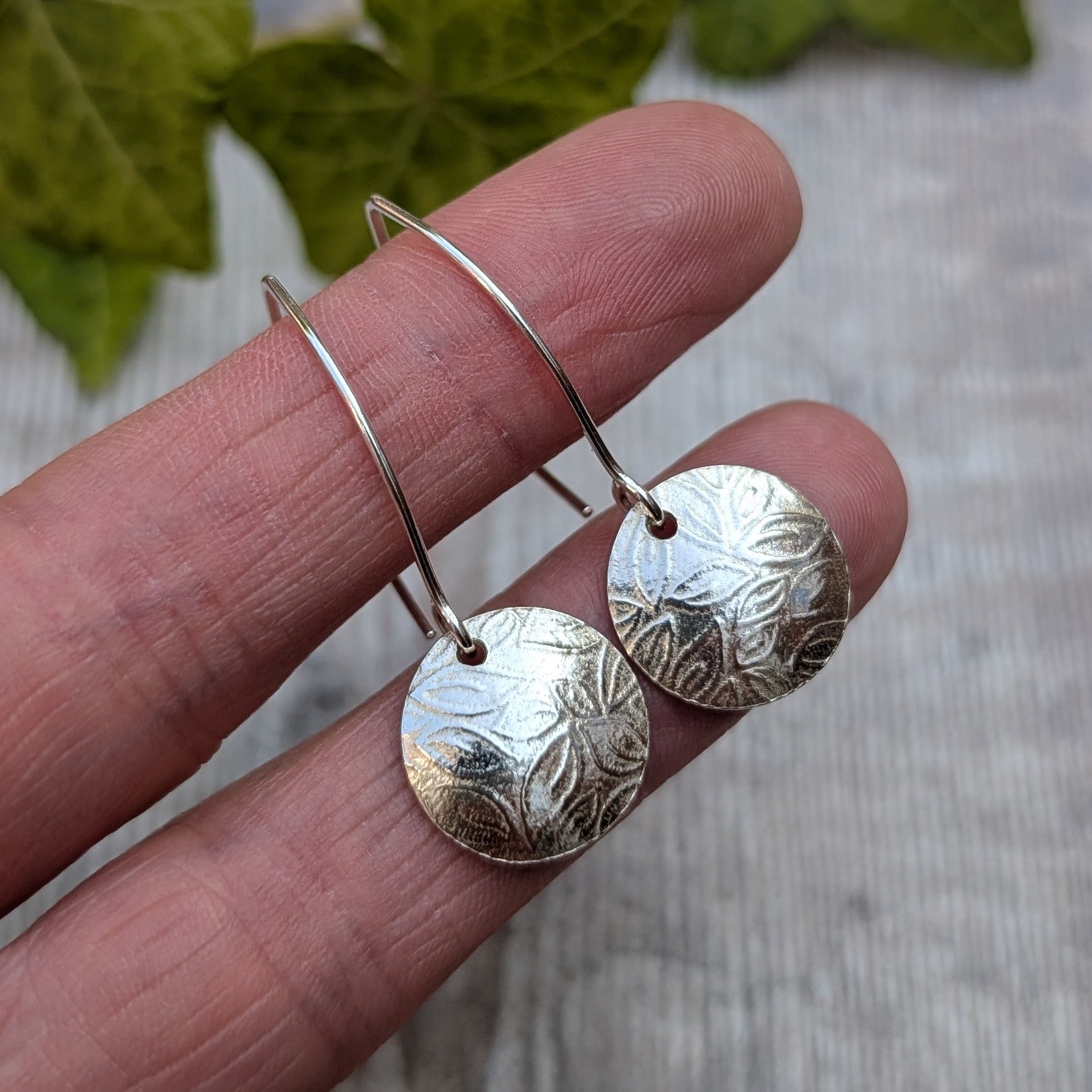 Close up of leaf pattern disc drop earrings handmade from recycled Sterling Silver highlighting the detailed leaf pattern and polished finish.
