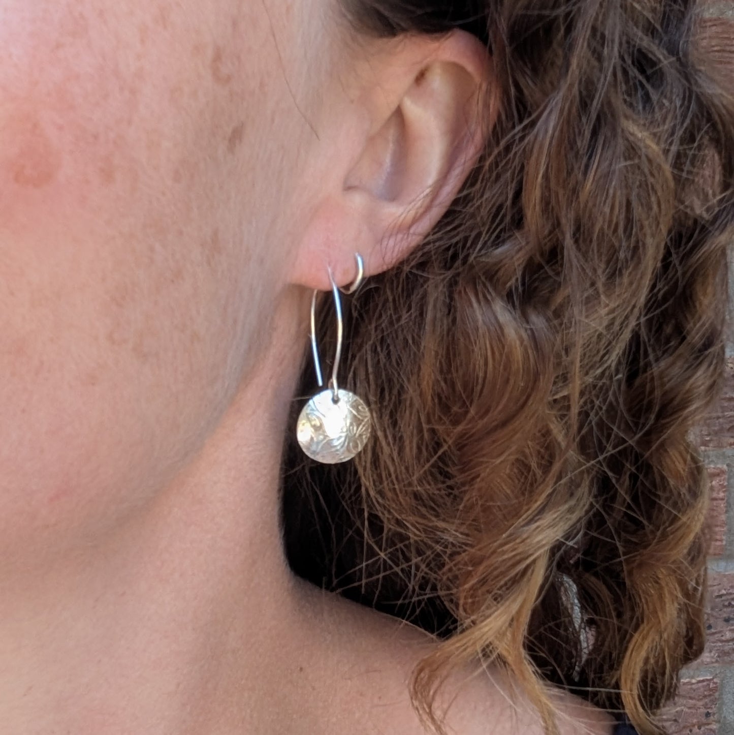 Leaf pattern disc drop earrings handmade from recycled Sterling Silver worn in the ear, showing their length and everyday style.