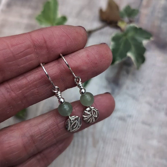 Video of Close up of green aventurine and silver leaf earrings held in a hand, showing the detailed leaf pattern on the recycled sterling silver discs and soft green aventurine beads.