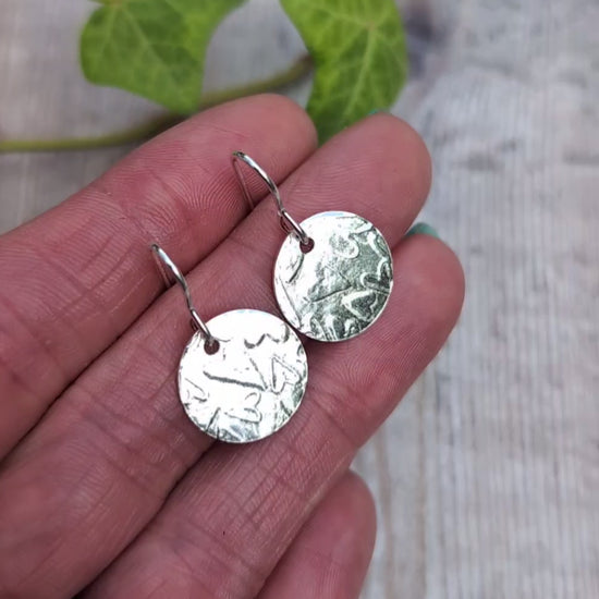 Video of Silver heart pattern disc earrings handmade from recycled Sterling Silver, held in a hand to show the heart patterned round discs.