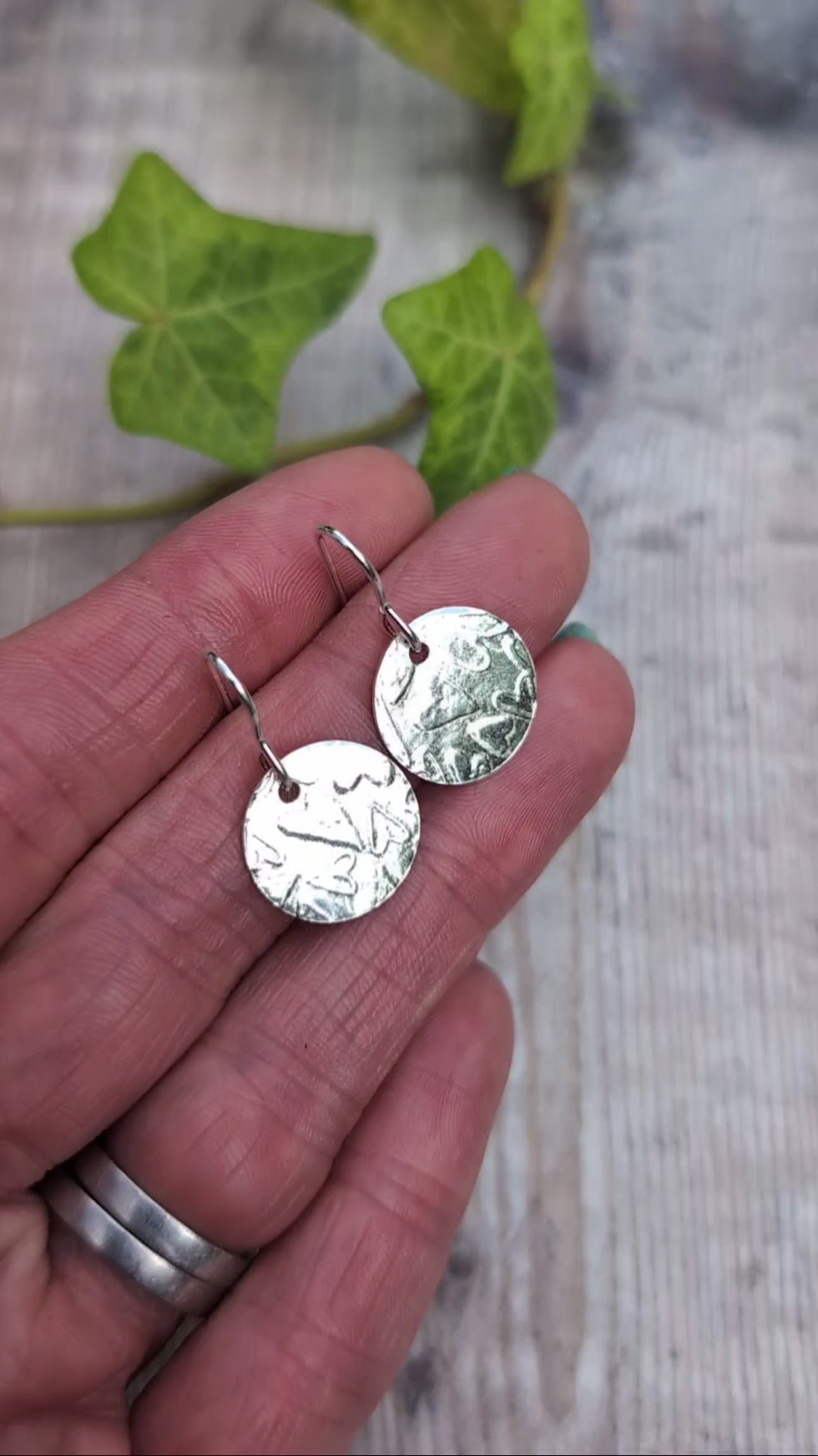 Video of Silver heart pattern disc earrings handmade from recycled Sterling Silver, held in a hand to show the heart patterned round discs.