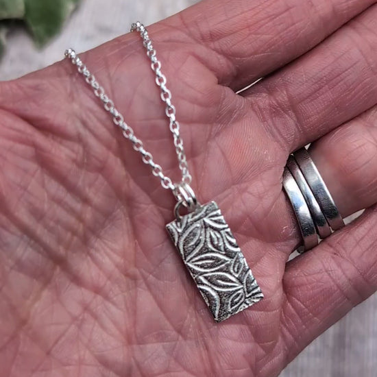 Video of Silver leaves rectangle necklace handmade from recycled Sterling Silver, shown resting in a hand to show the size and detailed leafy pattern.