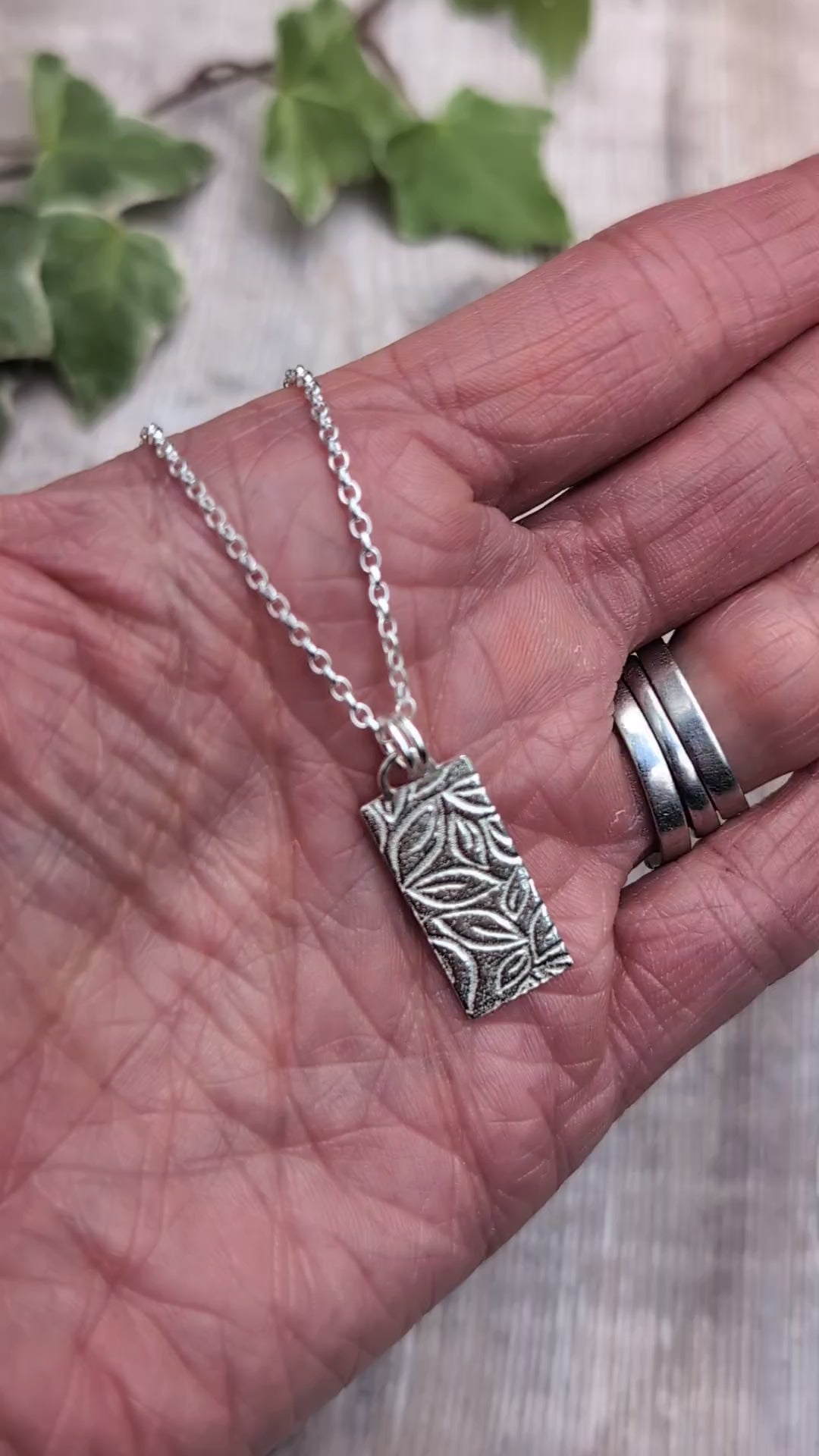 Video of Silver leaves rectangle necklace handmade from recycled Sterling Silver, shown resting in a hand to show the size and detailed leafy pattern.