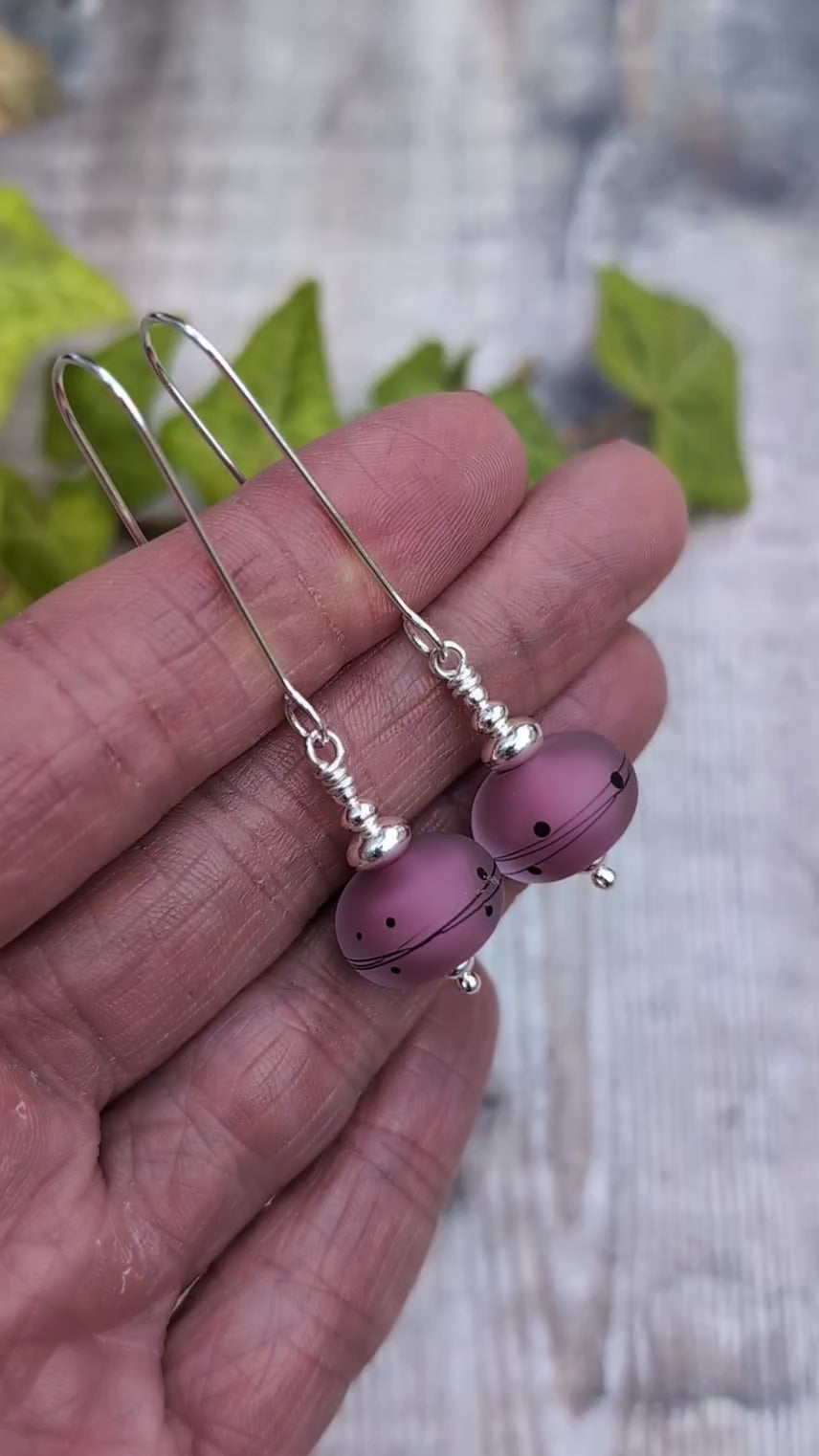 Video of pink scribbles lampwork glass long silver earrings held in a hand, showing the frosted pink beads with black scribble and dot patterns.