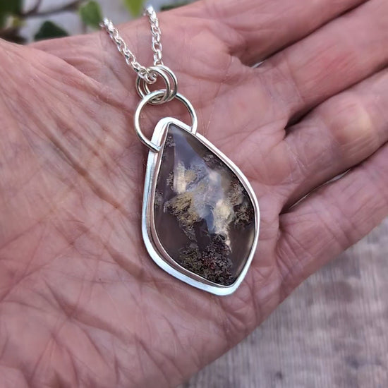 Video of Garden Moss Agate Statement Gemstone Necklace resting in an open hand, showing the handmade recycled sterling silver setting and large polished gemstone with natural earthy coloured patterns.