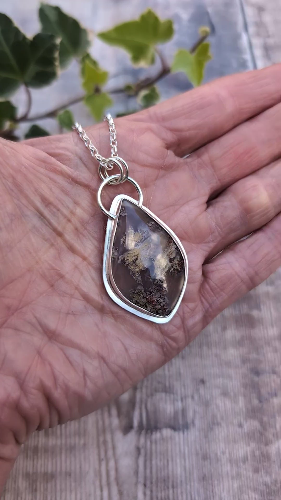 Video of Garden Moss Agate Statement Gemstone Necklace resting in an open hand, showing the handmade recycled sterling silver setting and large polished gemstone with natural earthy coloured patterns.