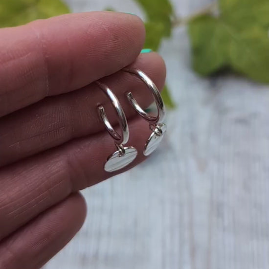Close up of silver disc drop hoop earrings handmade from recycled Sterling Silver, shown resting on fingertips to highlight the hand stamped wave pattern.