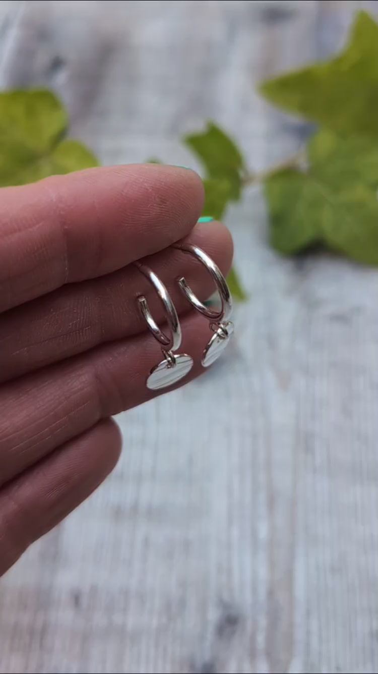 Close up of silver disc drop hoop earrings handmade from recycled Sterling Silver, shown resting on fingertips to highlight the hand stamped wave pattern.