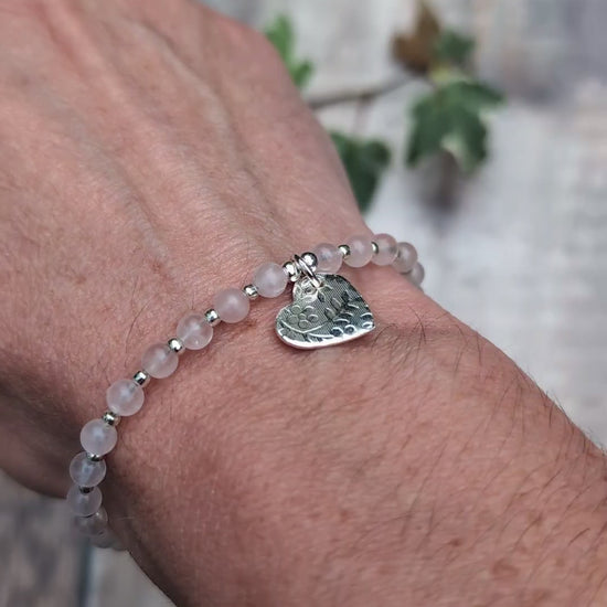 Video of Rose quartz and silver floral heart charm bracelet being worn on a wrist, showing the textured silver heart charm hanging from the soft pink rose quartz beads.