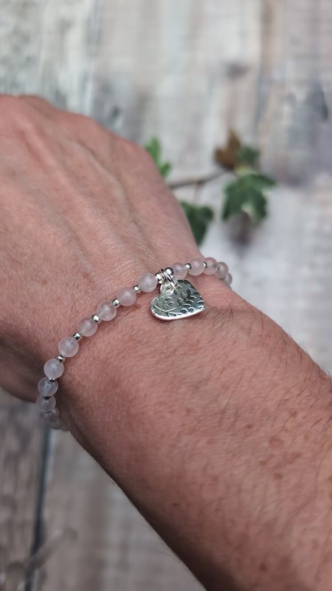 Video of Rose quartz and silver floral heart charm bracelet being worn on a wrist, showing the textured silver heart charm hanging from the soft pink rose quartz beads.