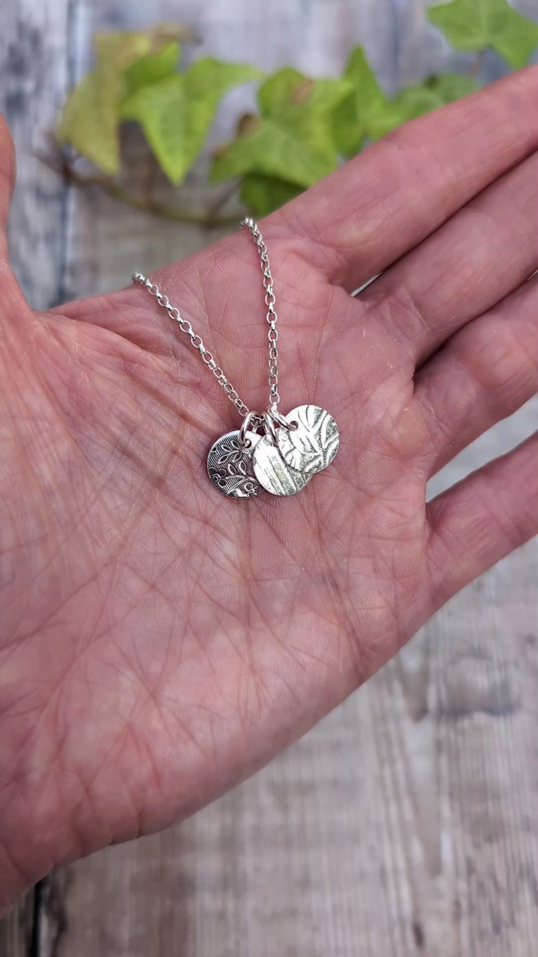 Video of Silver wildflower trio of discs necklace handmade from recycled Sterling Silver, shown resting in a hand with three different patterned silver discs.