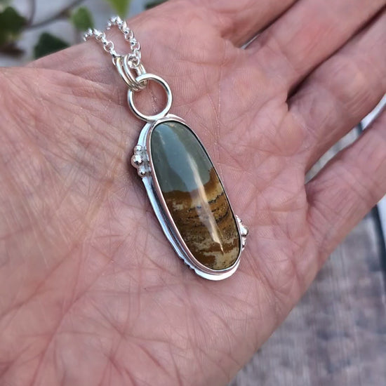 Video of Owyhee Picture Jasper Statement Gemstone Necklace resting in the palm of a hand, showing the size of the long oval gemstone and handmade Sterling Silver setting.