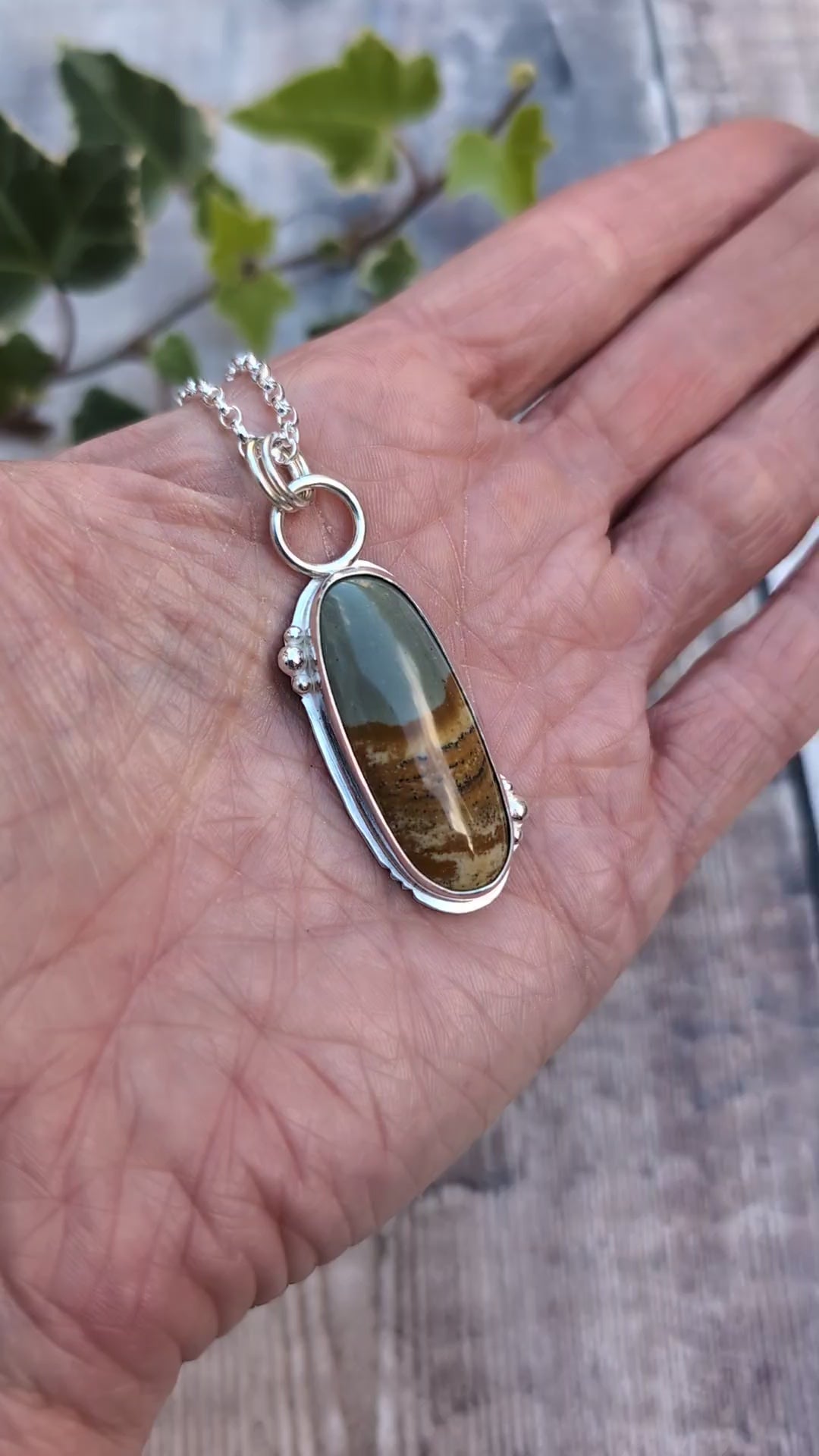Video of Owyhee Picture Jasper Statement Gemstone Necklace resting in the palm of a hand, showing the size of the long oval gemstone and handmade Sterling Silver setting.